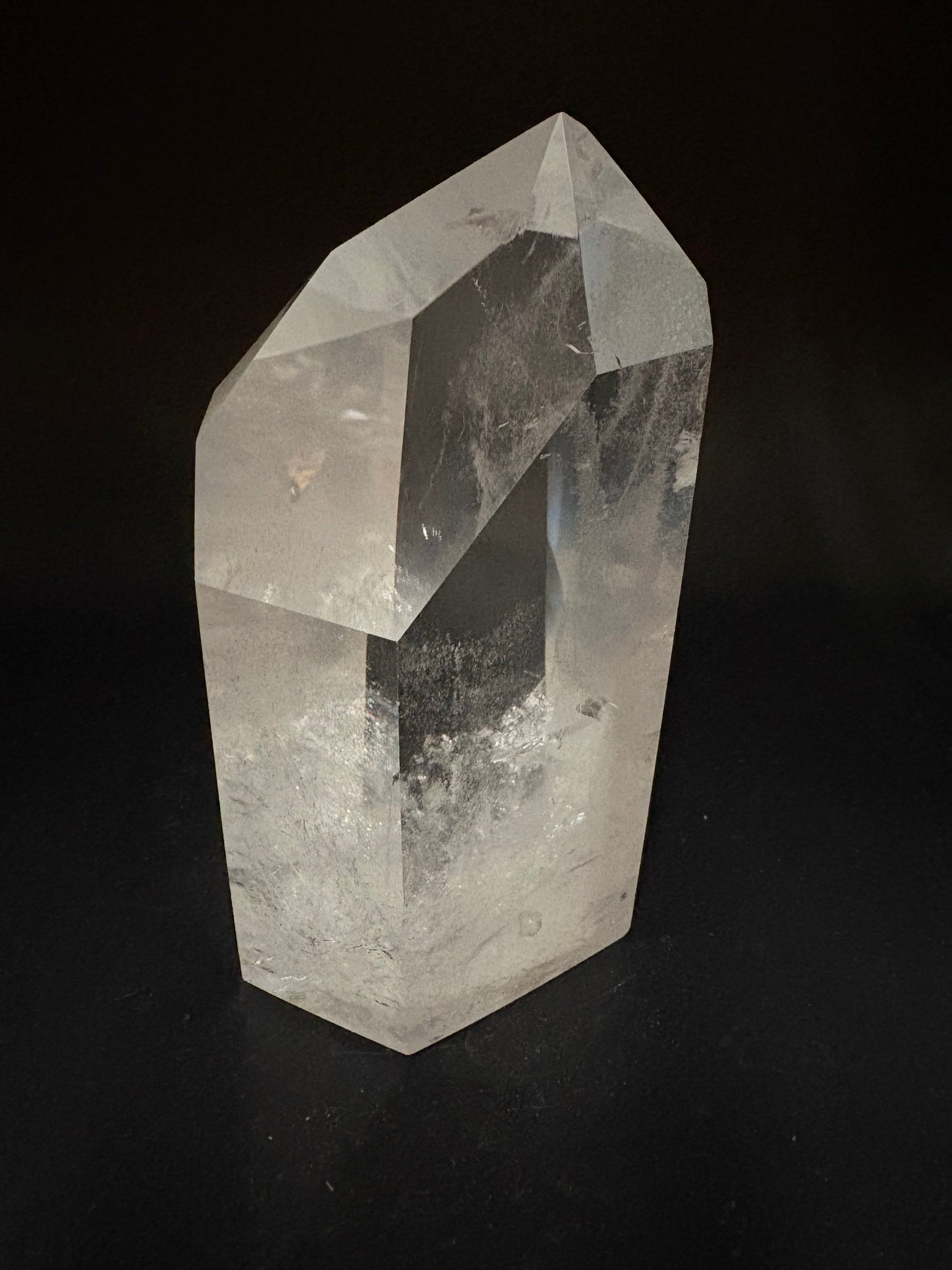 A natural clear quartz crystal point with faceted edges and internal inclusions, photographed on a solid black background.
