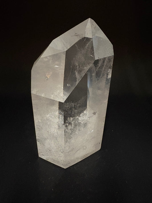 A natural clear quartz crystal point with faceted edges and internal inclusions, photographed on a solid black background.