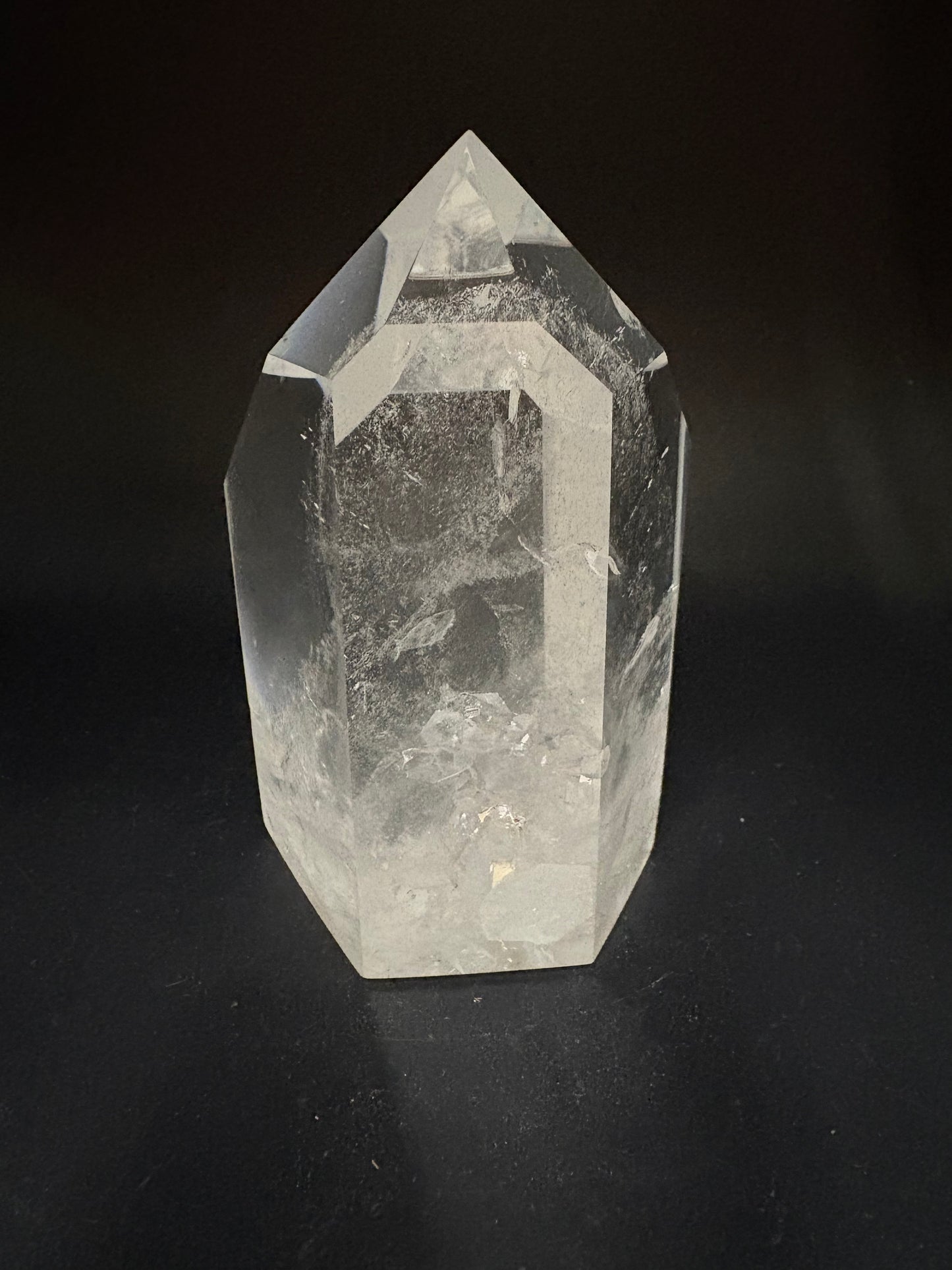 A clear quartz crystal point with natural inclusions, photographed on a dark black background.