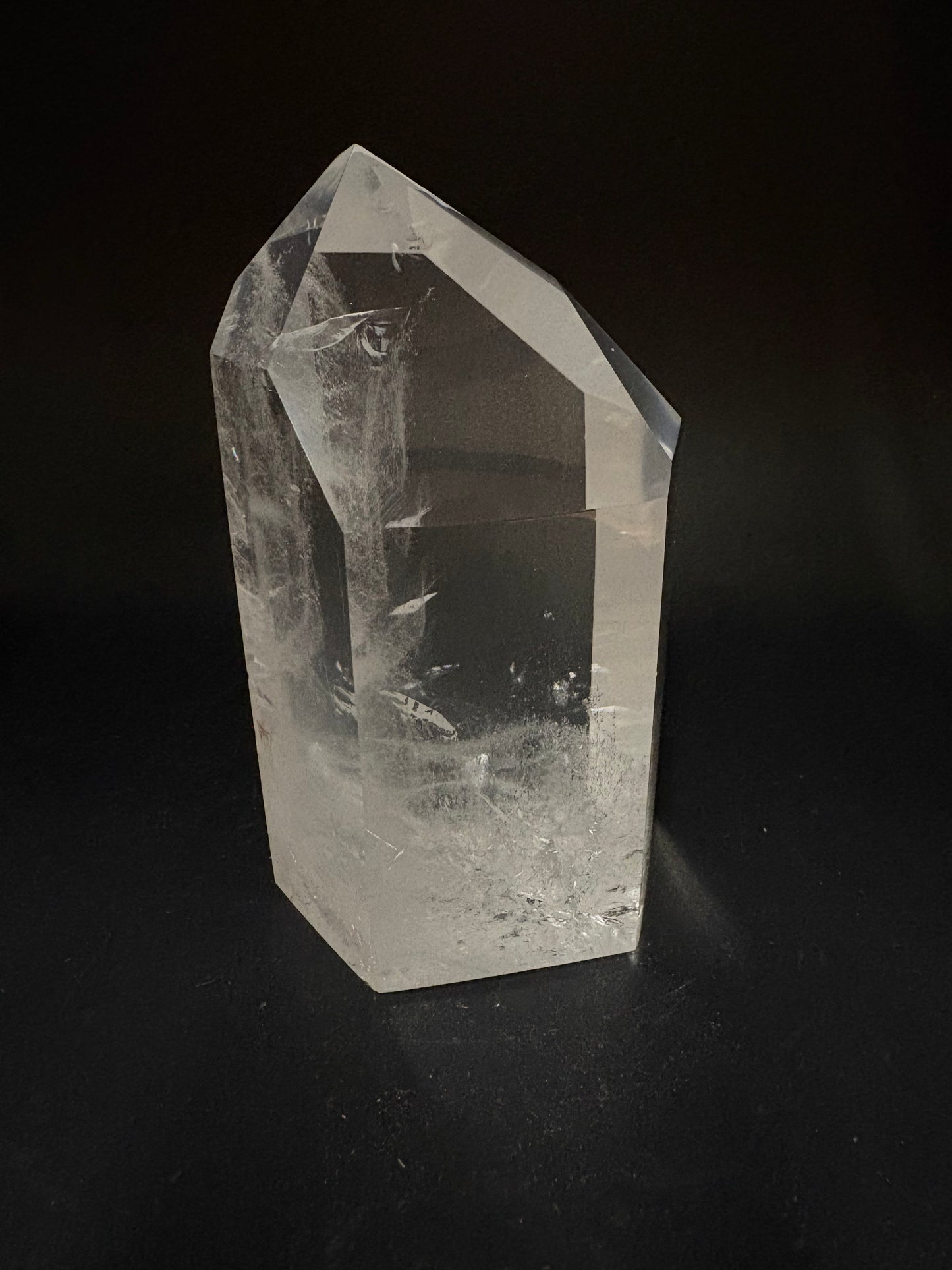A clear quartz crystal point with natural inclusions, photographed on a dark black background.