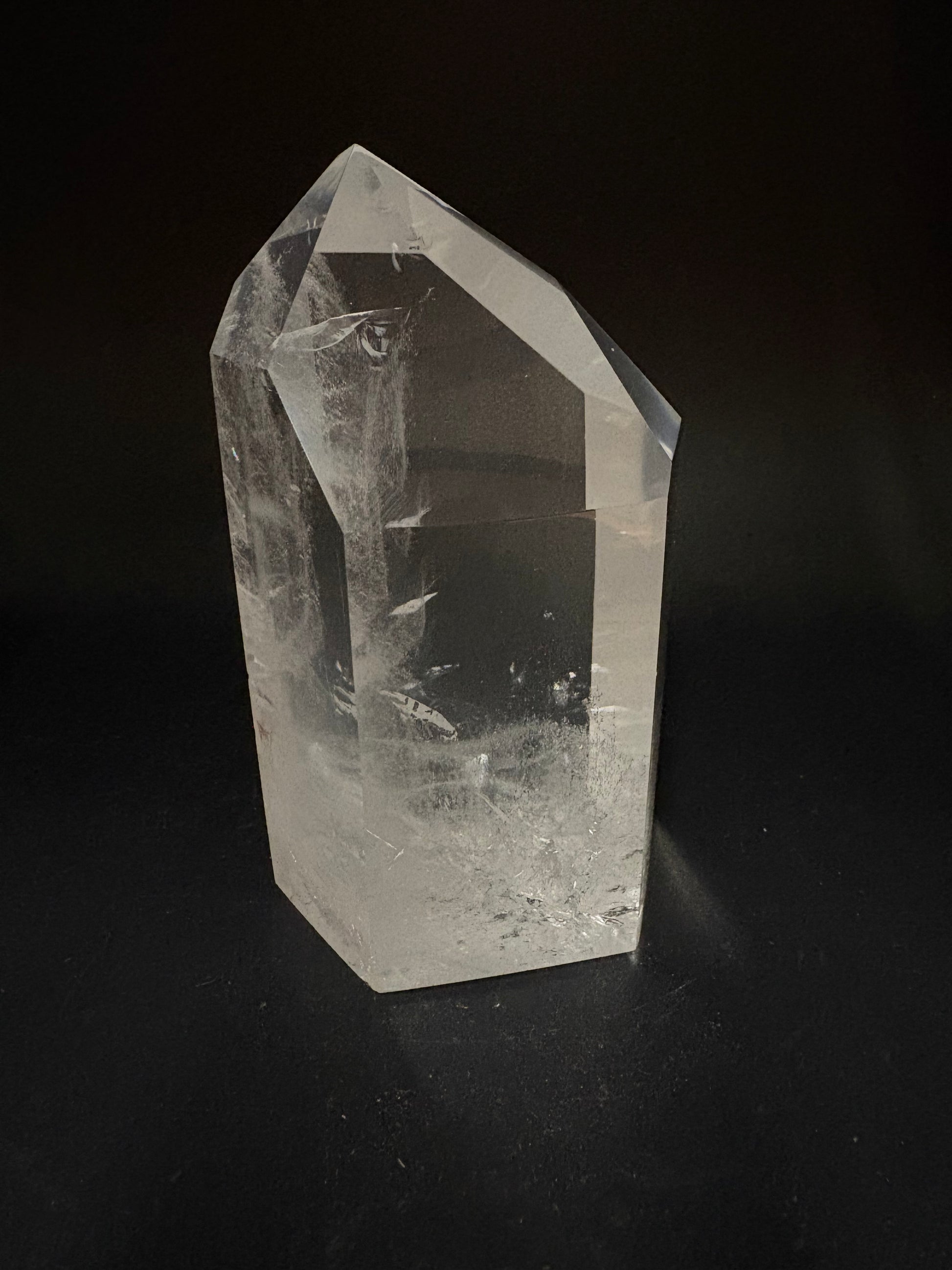 A clear quartz crystal point with natural inclusions, photographed on a dark black background.