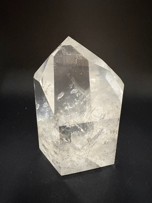 A faceted clear quartz crystal point with natural inclusions, displayed on a dark black background.