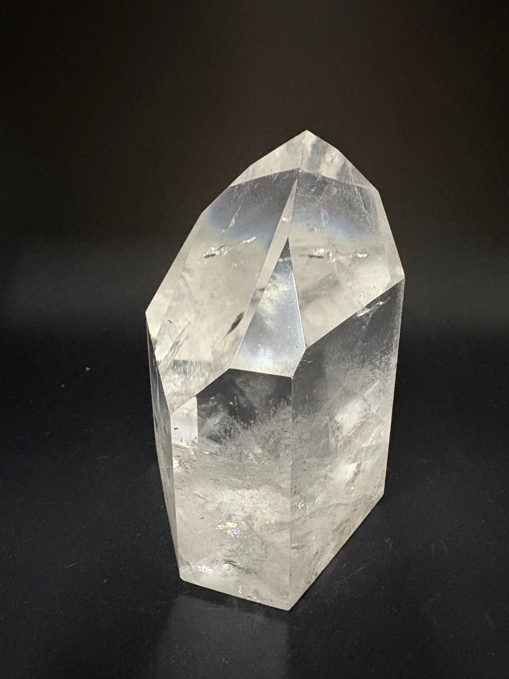 A faceted clear quartz crystal point with natural inclusions, photographed on a dark black background.