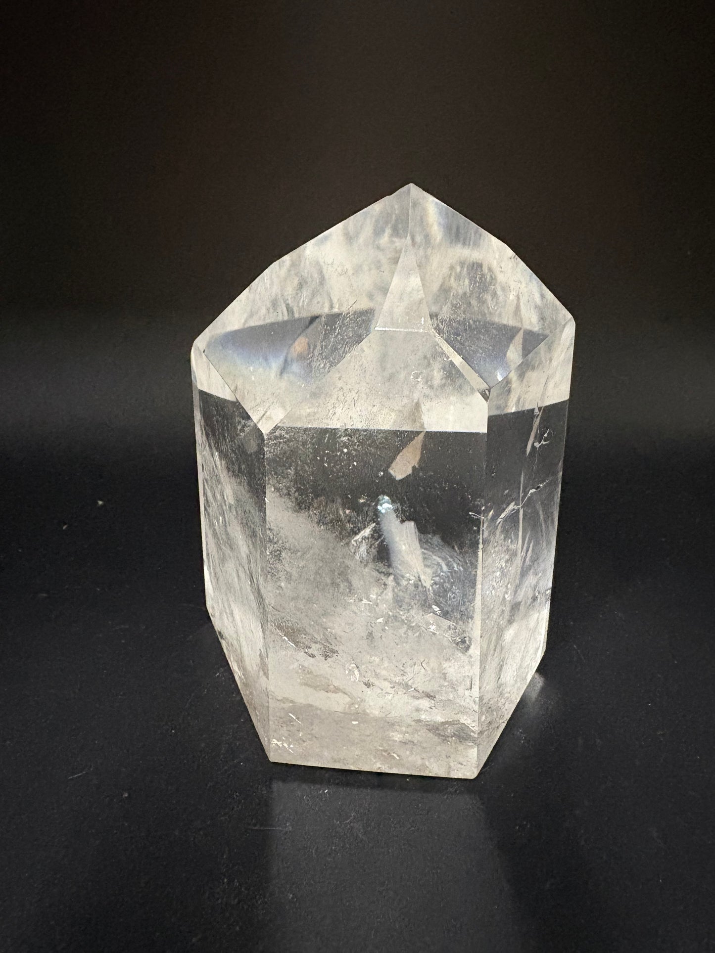 A clear faceted crystal point, likely quartz, with natural inclusions and internal fractures, photographed on a dark black background.
