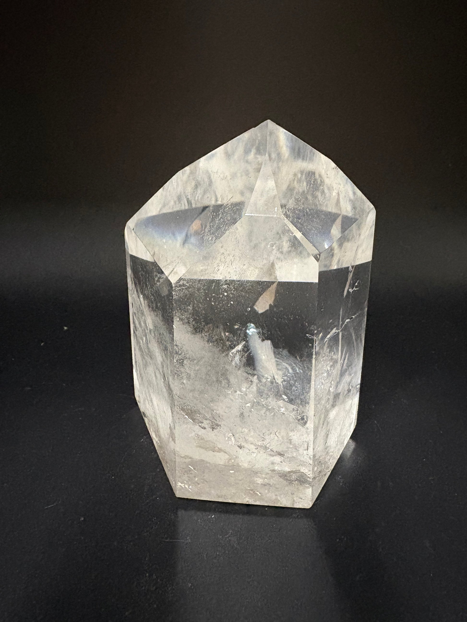 A clear faceted crystal point, likely quartz, with natural inclusions and internal fractures, photographed on a dark black background.