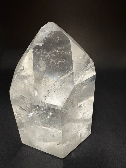 A large, faceted clear quartz crystal with natural inclusions, displayed on a solid black background.