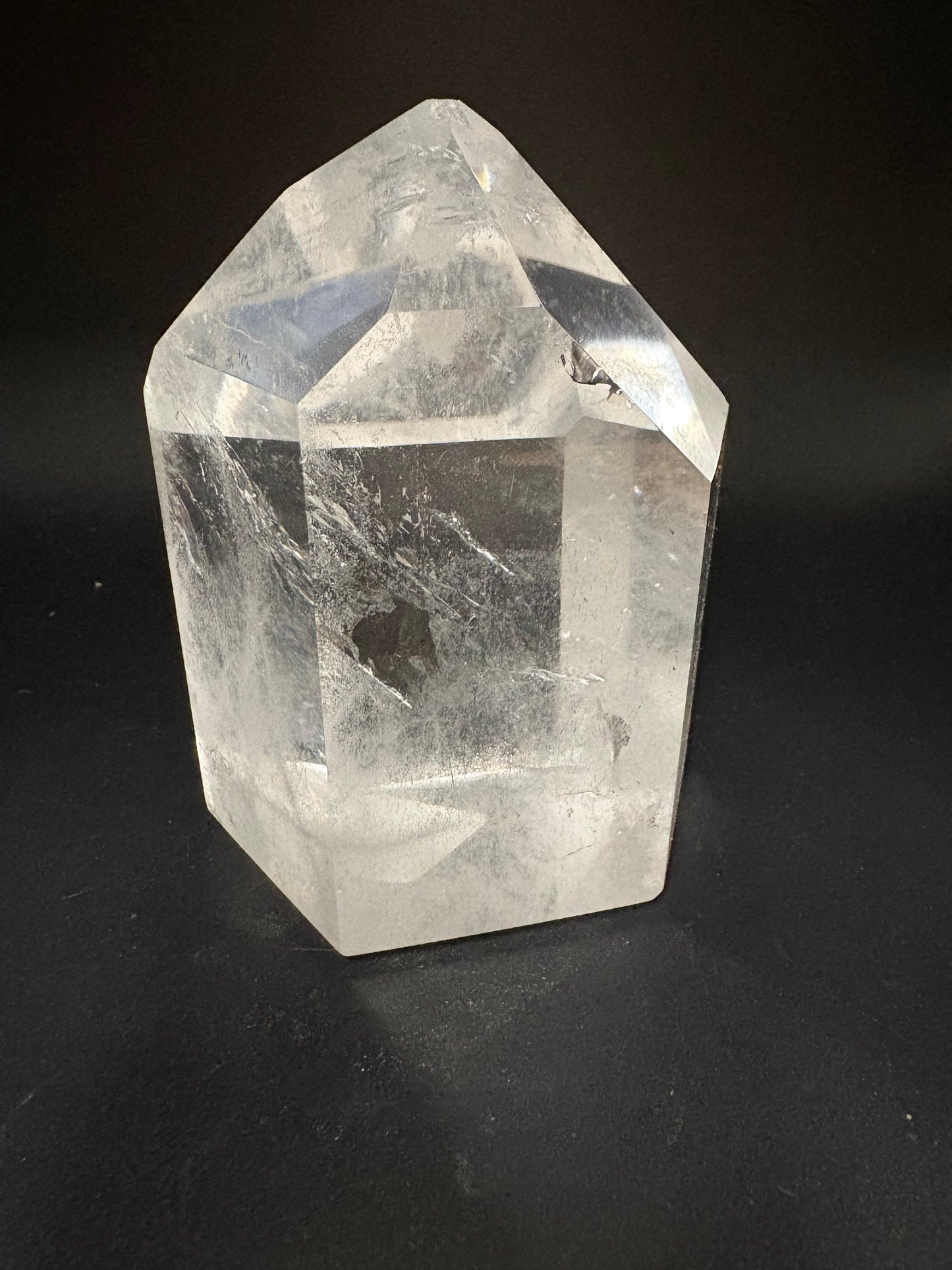 A clear faceted crystal stone with a pointed hexagonal shape, resting on a dark black background.