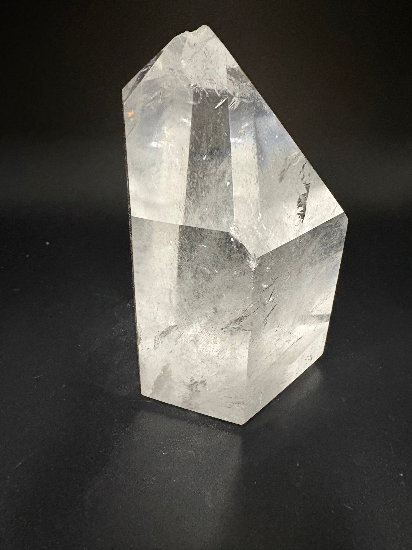 A clear faceted crystal point, likely quartz, resting on a dark black background.