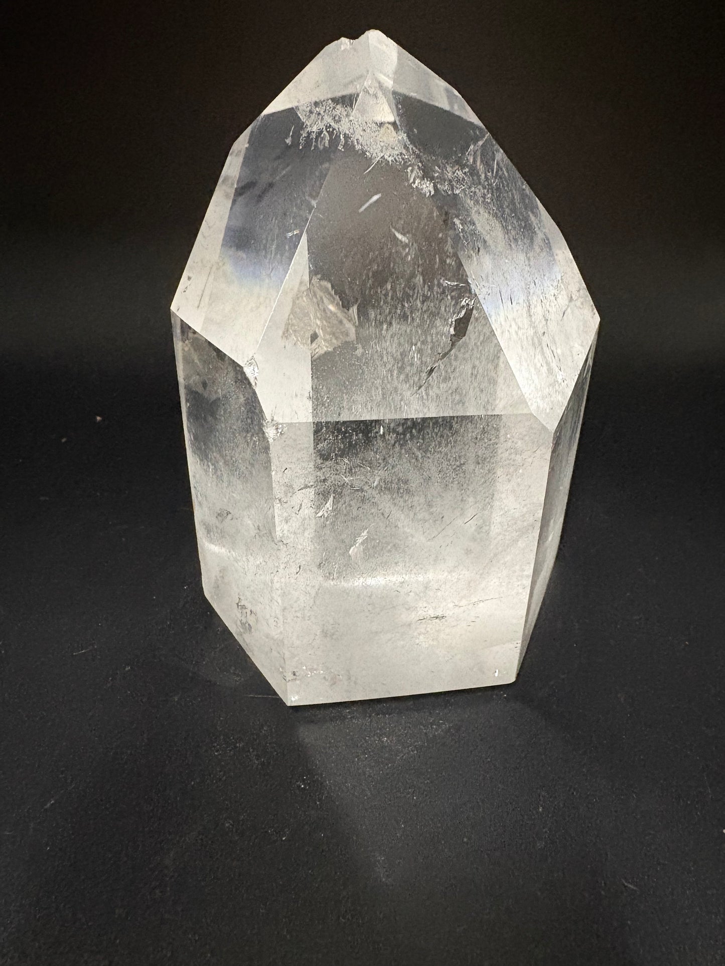 A faceted clear crystal point, quartz, displayed on a dark black background.
