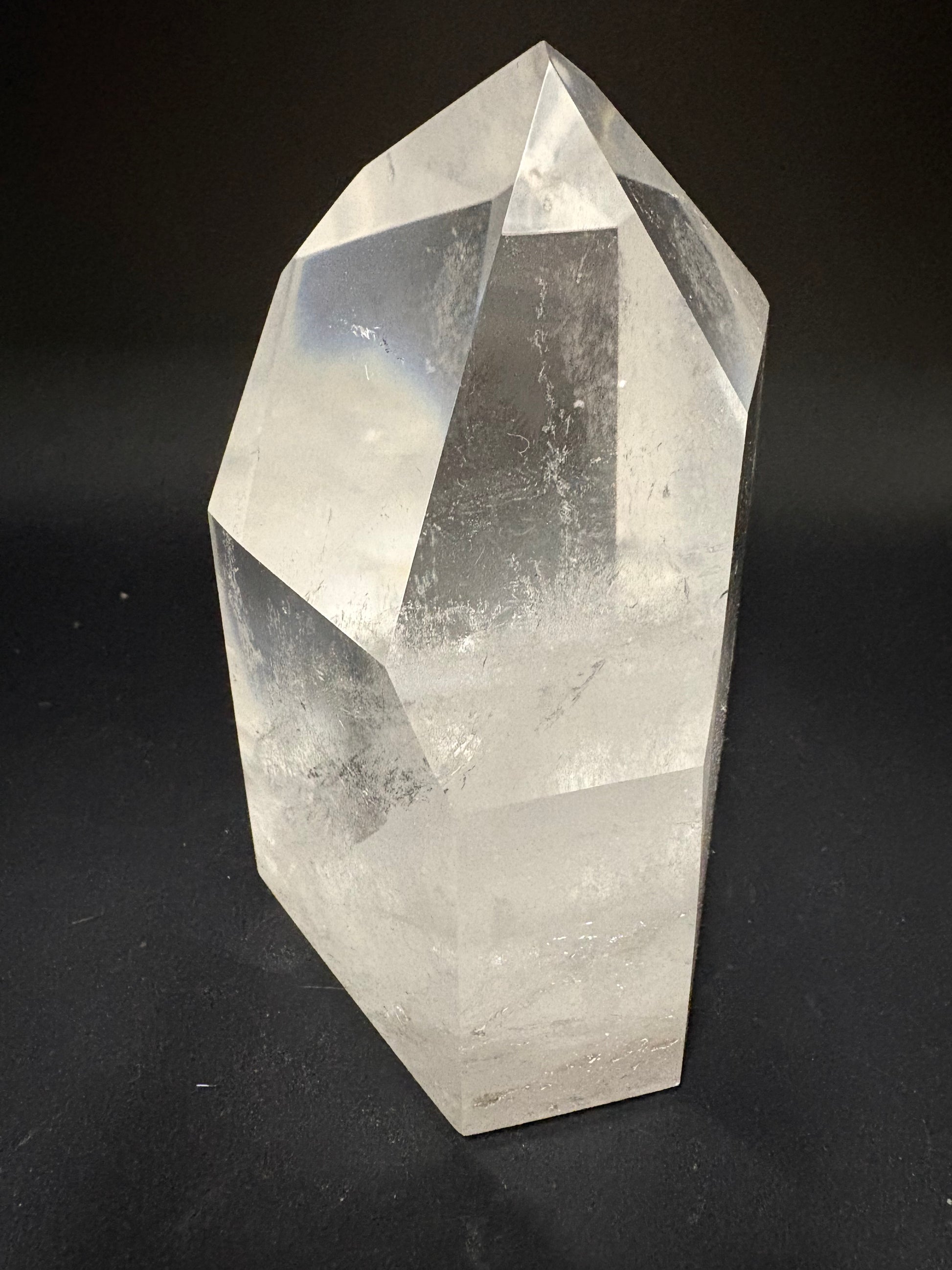 A clear faceted crystal point, likely quartz, displayed on a dark black background.