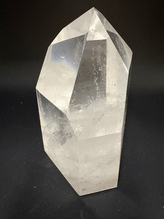A clear faceted crystal point, likely quartz, displayed on a dark black background.
