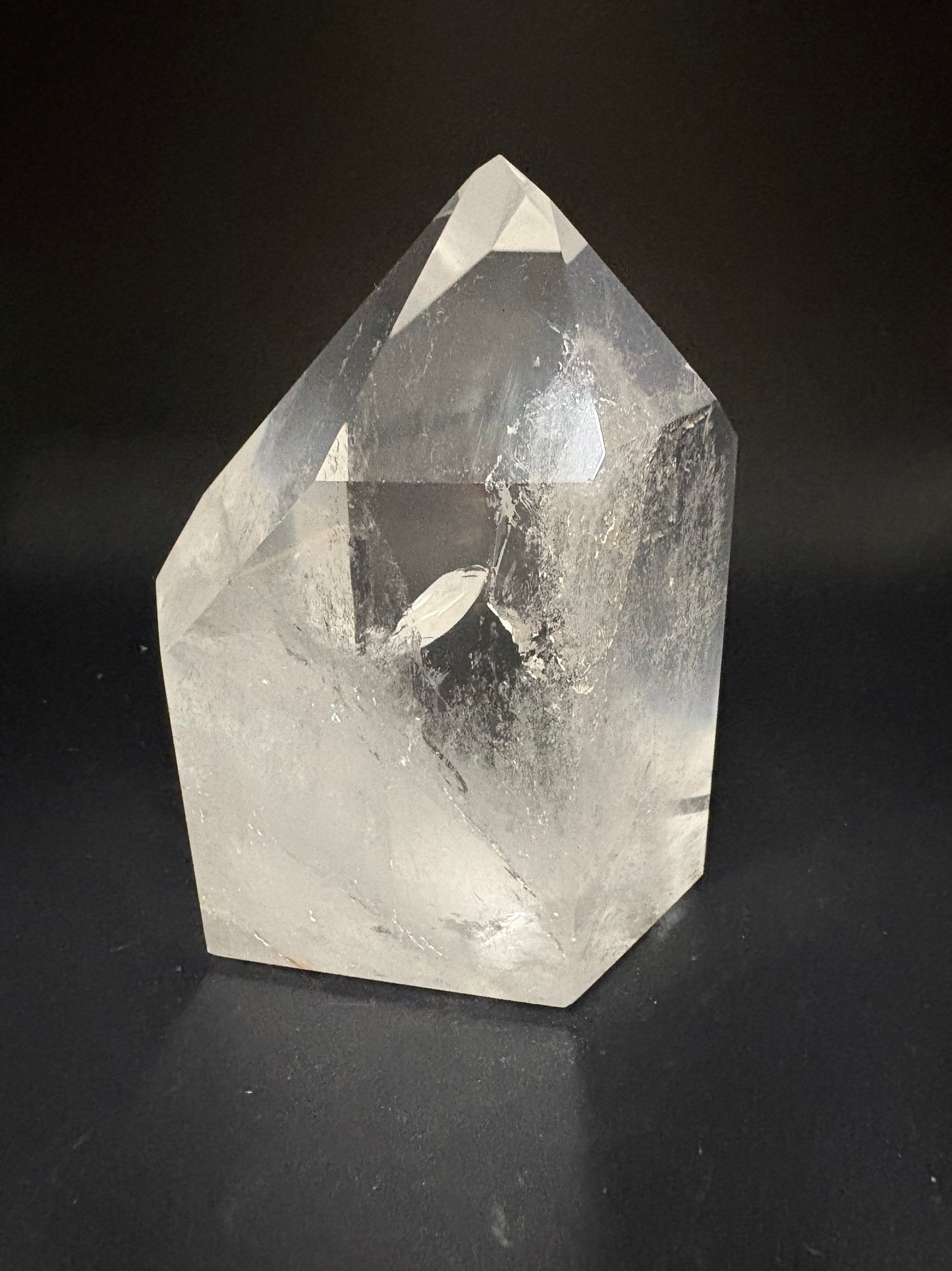 A faceted clear quartz crystal point, showing natural internal inclusions and striations, photographed on a dark black background.