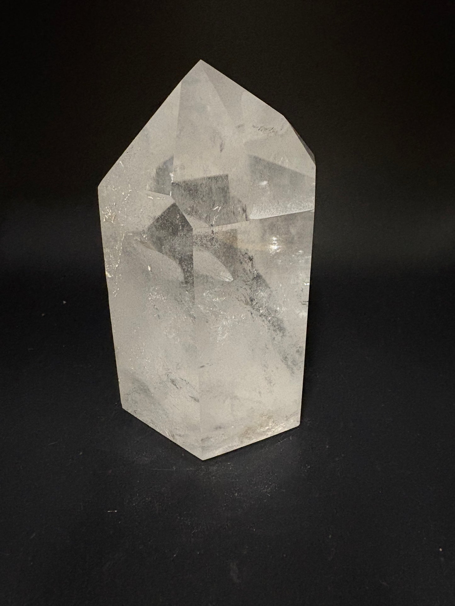 A faceted clear quartz crystal point with natural inclusions, displayed on a solid black background.