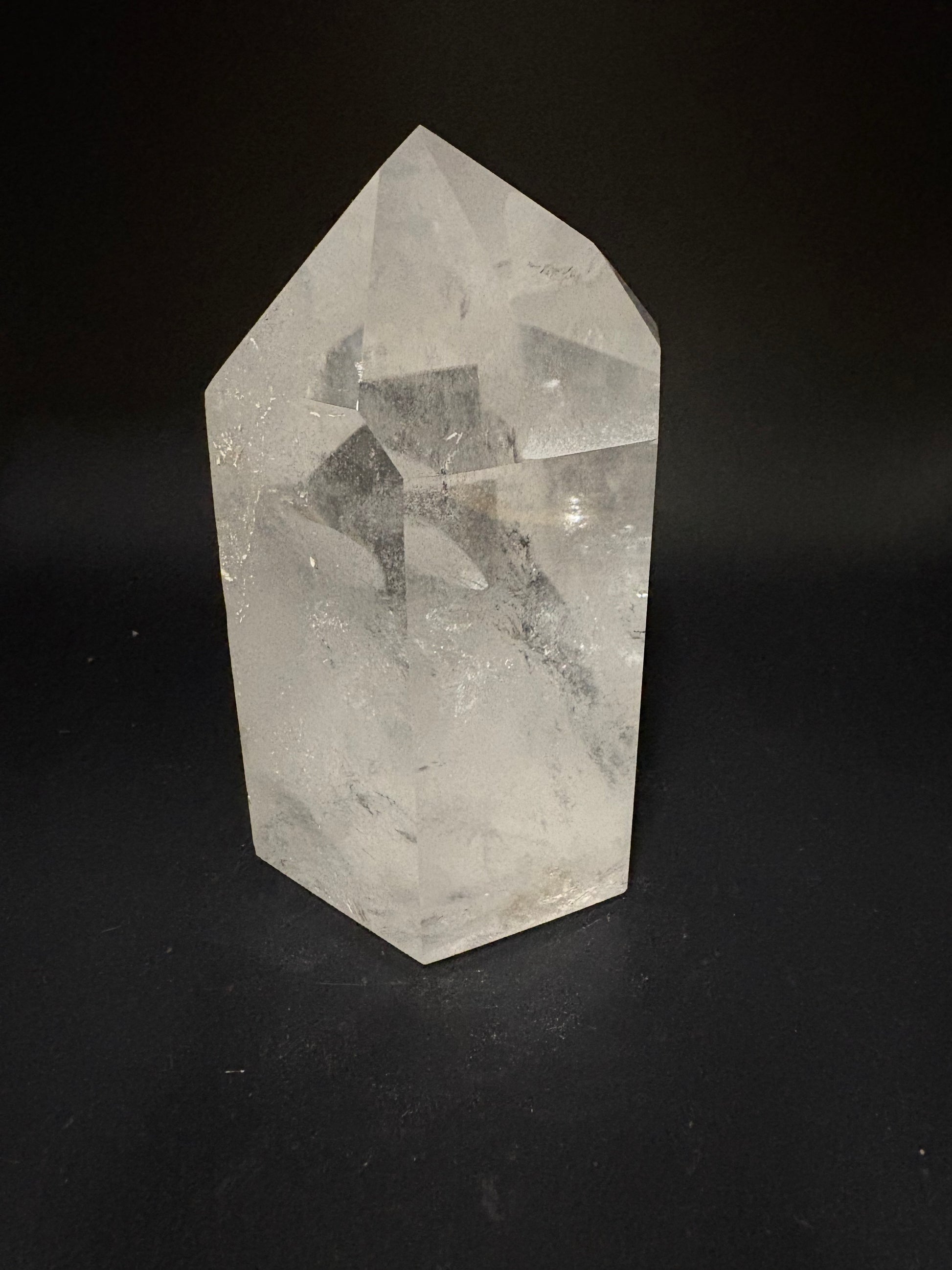 A faceted clear quartz crystal point with natural inclusions, displayed on a solid black background.