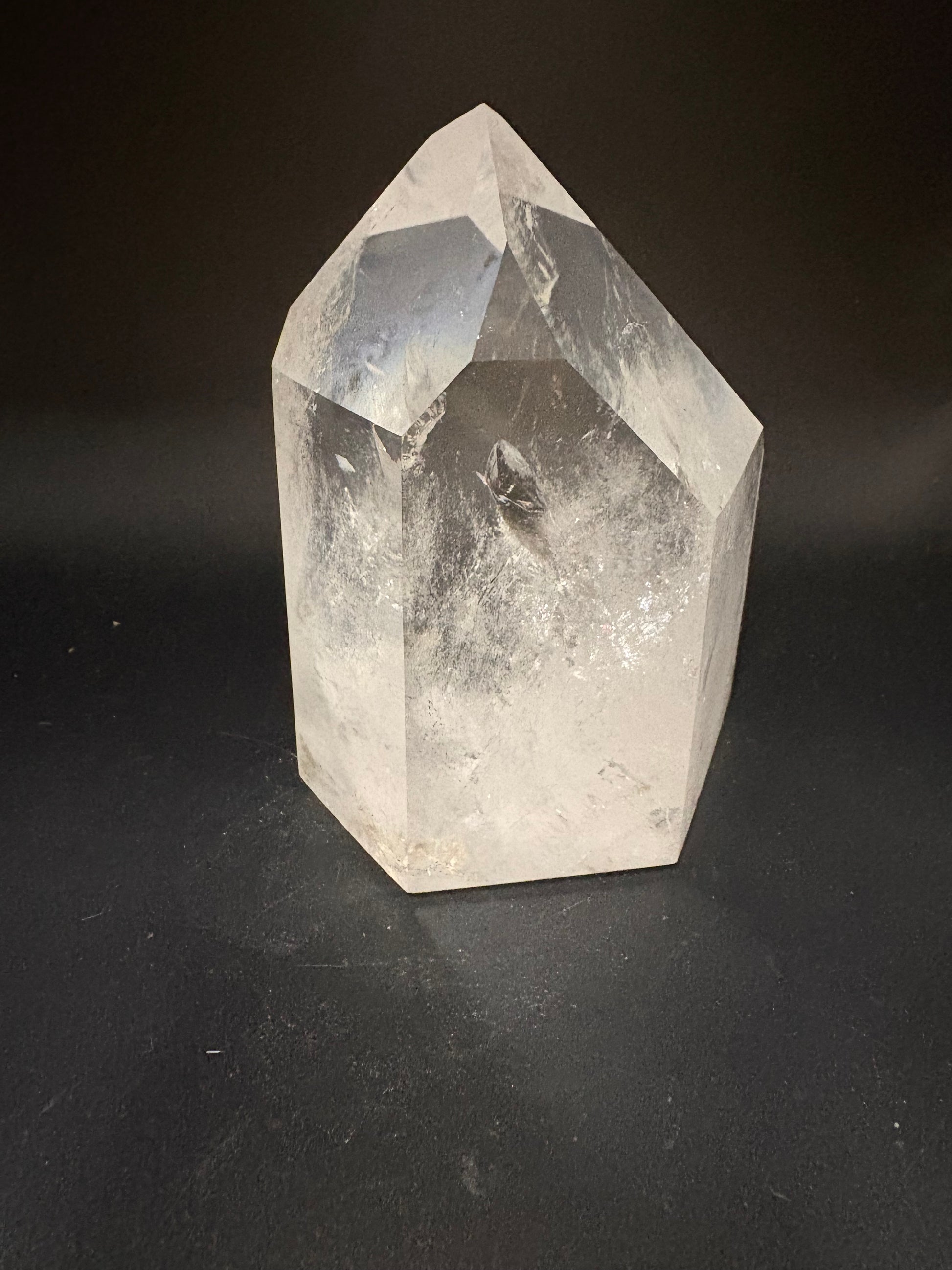 A faceted clear crystal stone, likely quartz, resting on a dark black background.