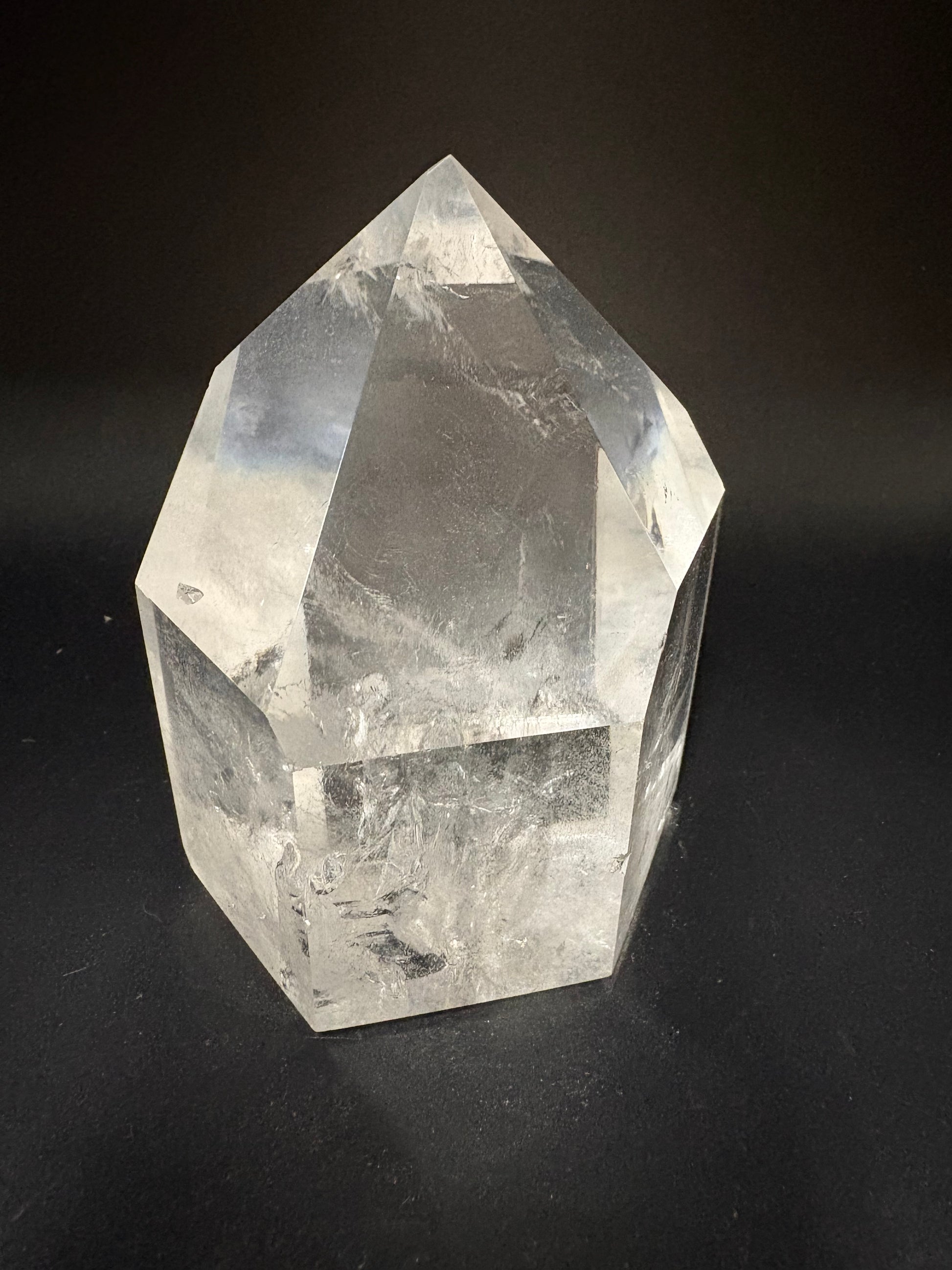 A clear faceted crystal point, resembling a quartz point, photographed on a dark black background.