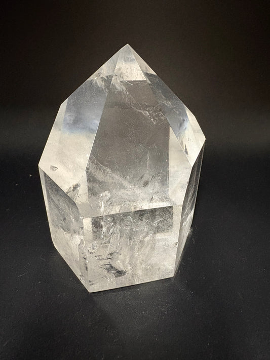 A clear faceted crystal point, resembling a quartz point, photographed on a dark black background.