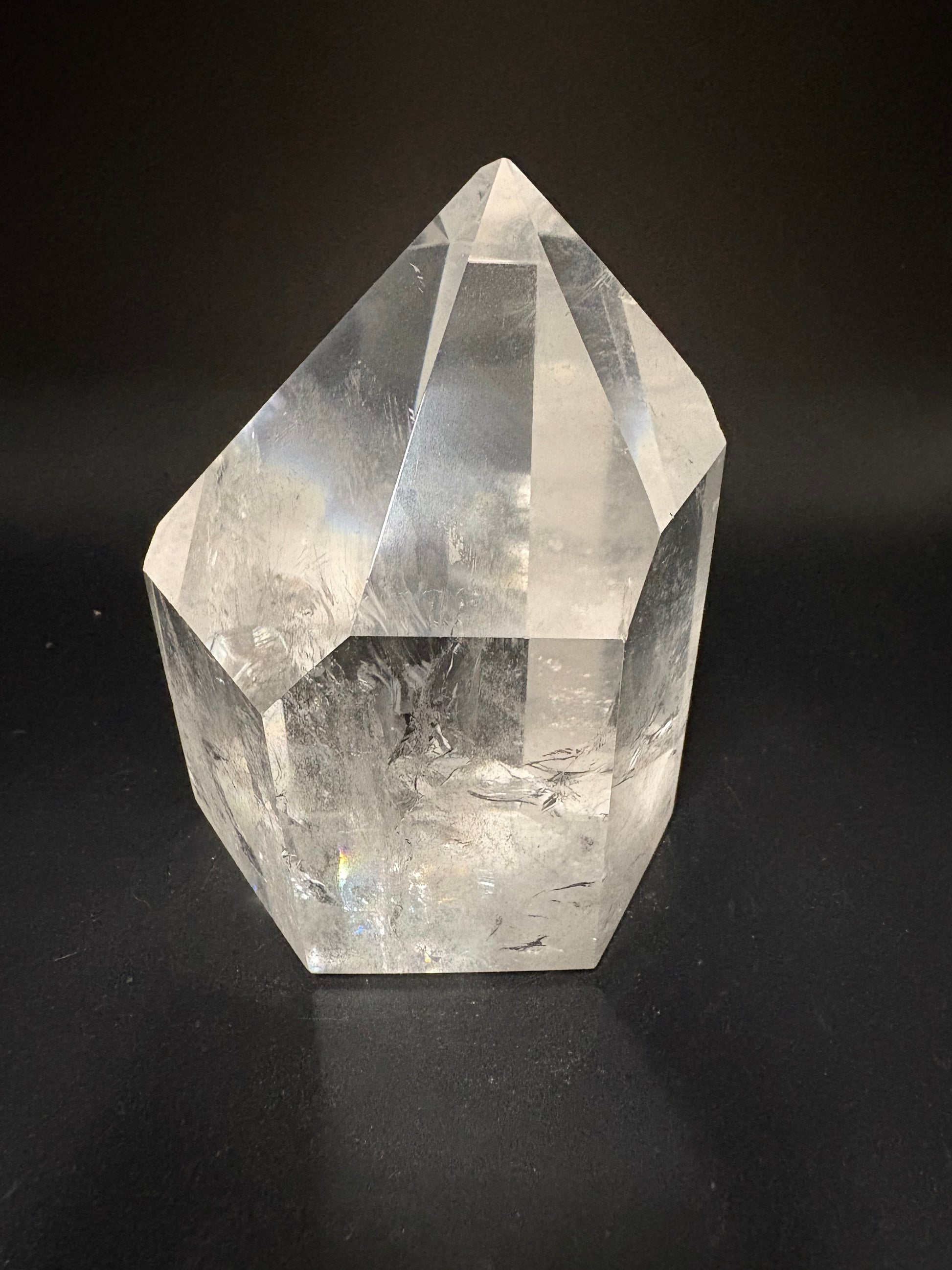 A clear faceted crystal point, likely quartz, displayed on a dark black background.