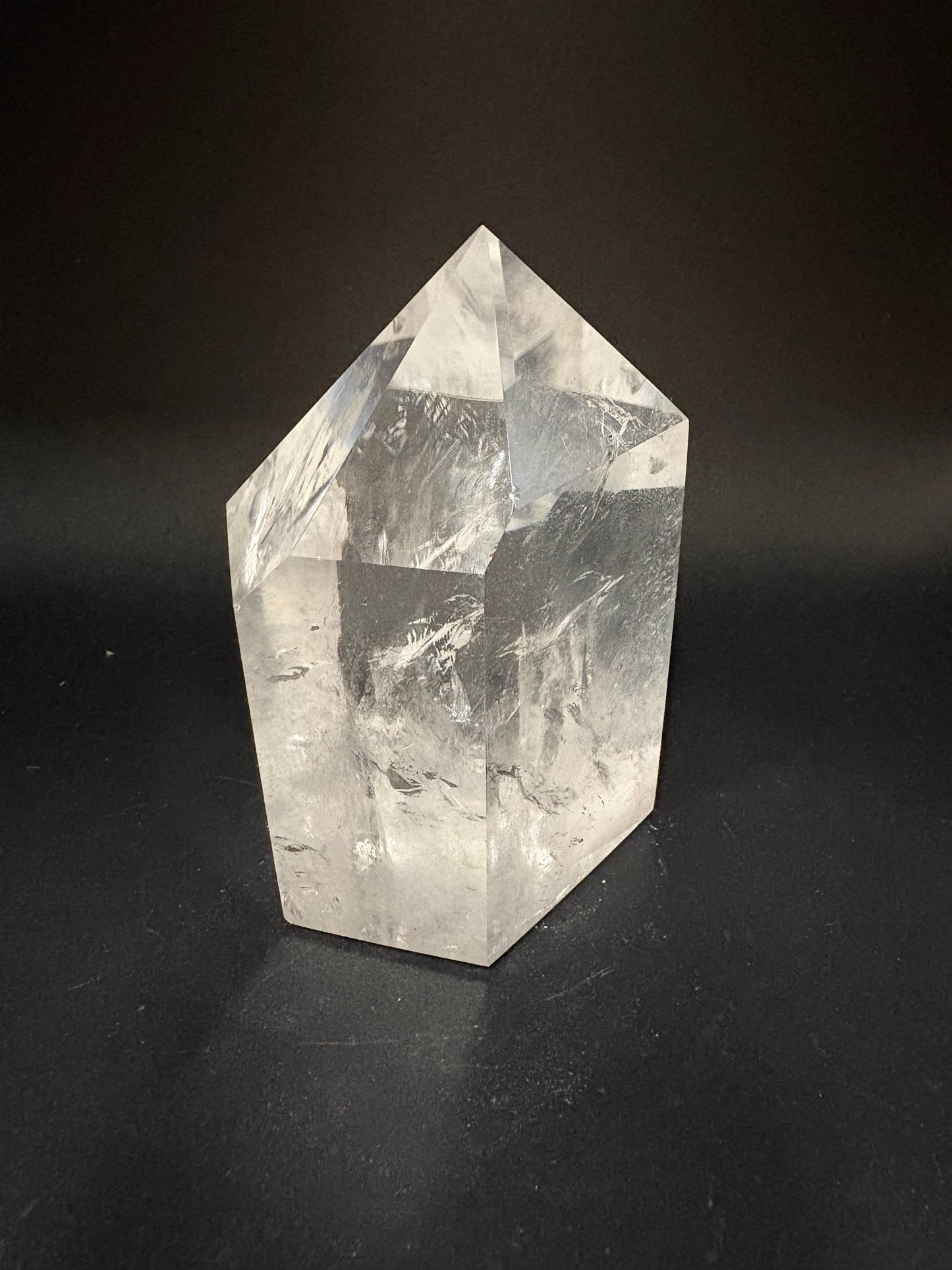 A clear faceted crystal point, likely quartz, displayed on a dark black background.