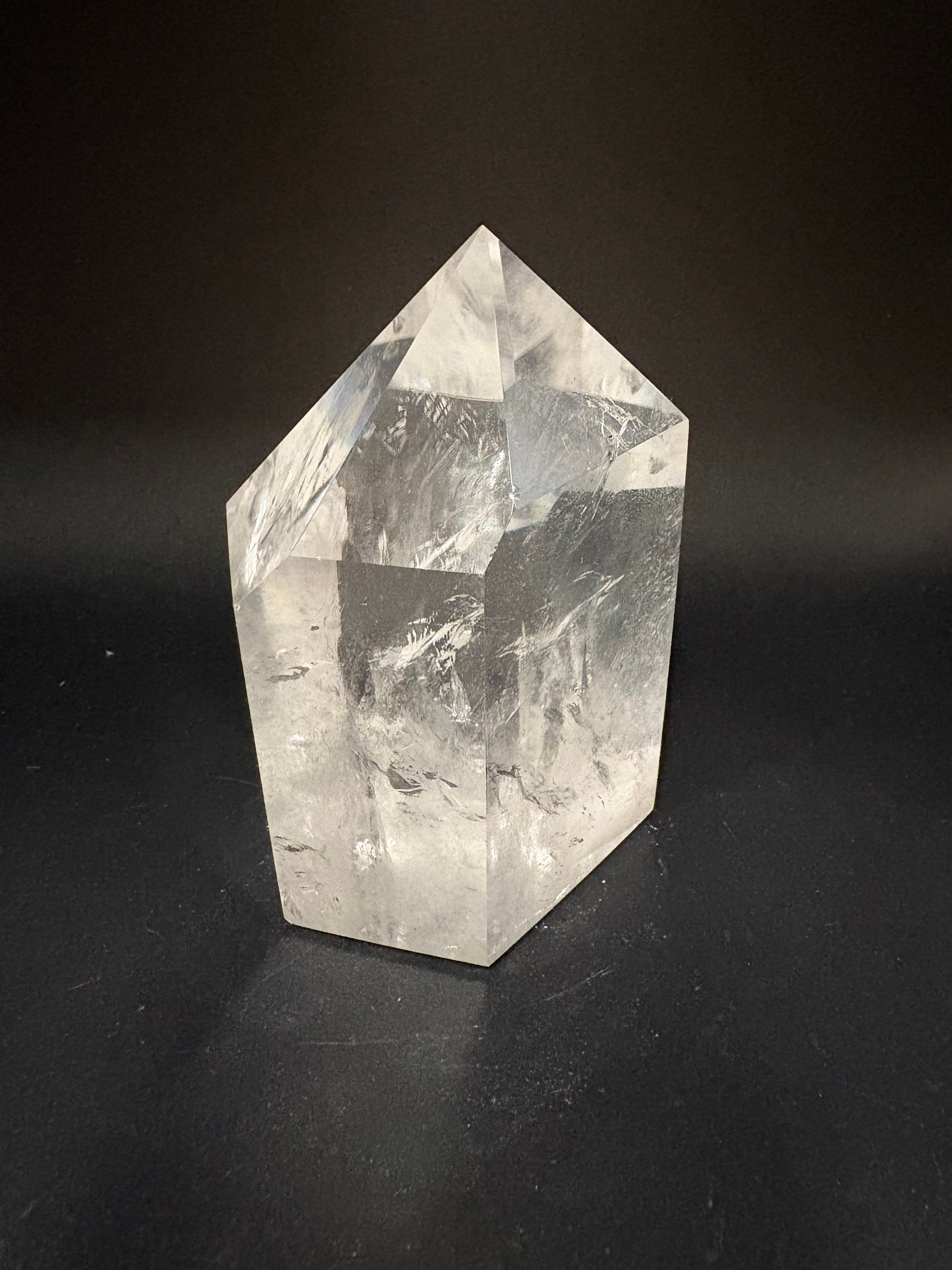 A clear faceted crystal point, likely quartz, displayed on a dark black background.