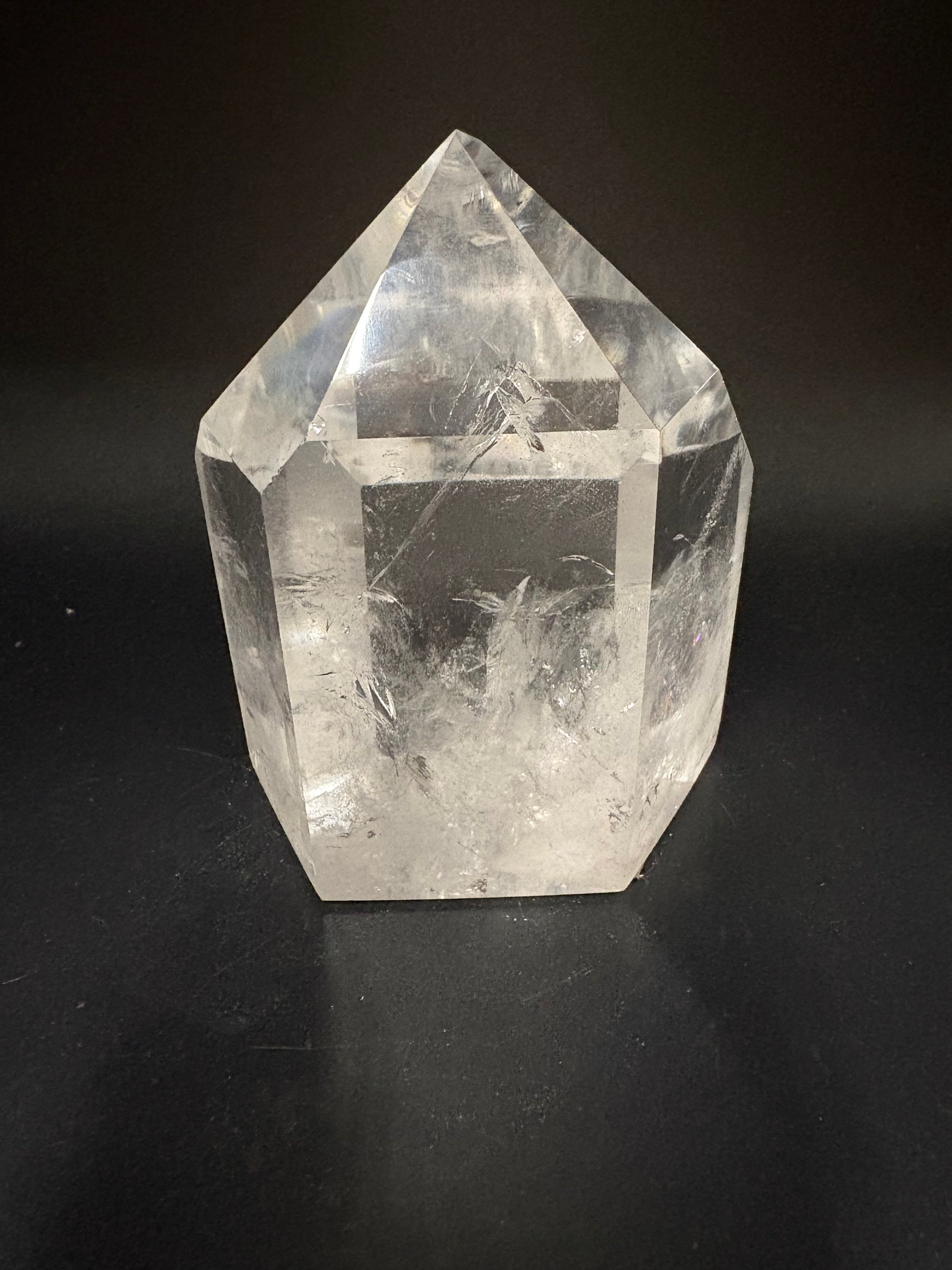 A clear quartz crystal point with natural inclusions, photographed on a dark black background.