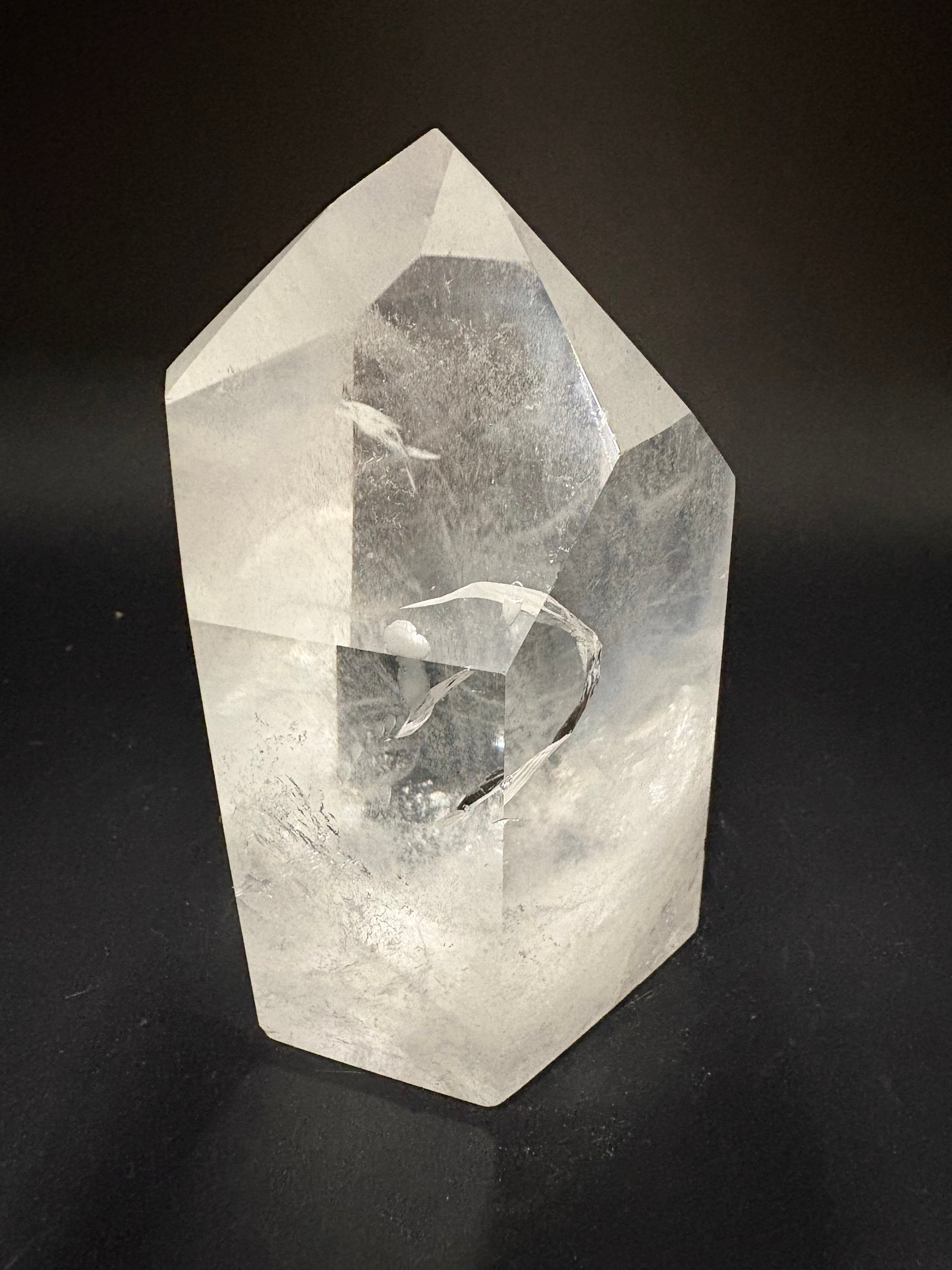 A faceted clear crystal stone, likely a quartz point, displayed on a dark black background.