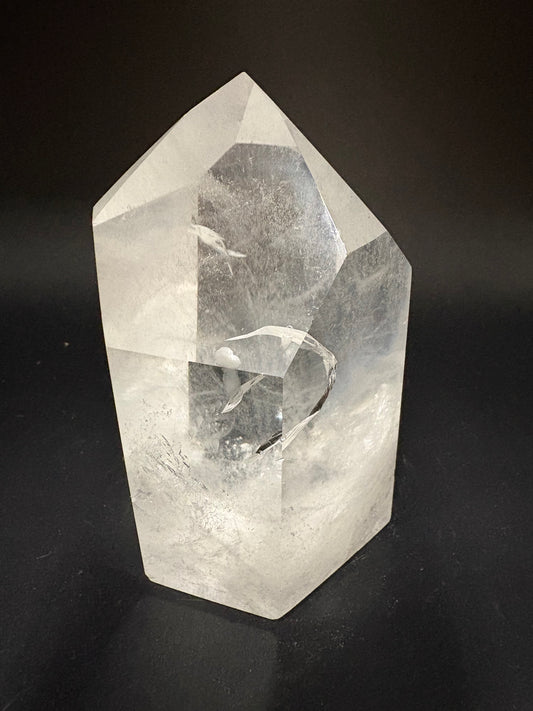 A faceted clear crystal stone, likely a quartz point, displayed on a dark black background.