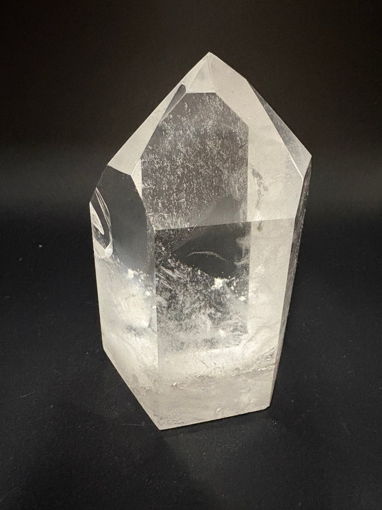 A clear quartz crystal point with natural inclusions, photographed on a dark black background.