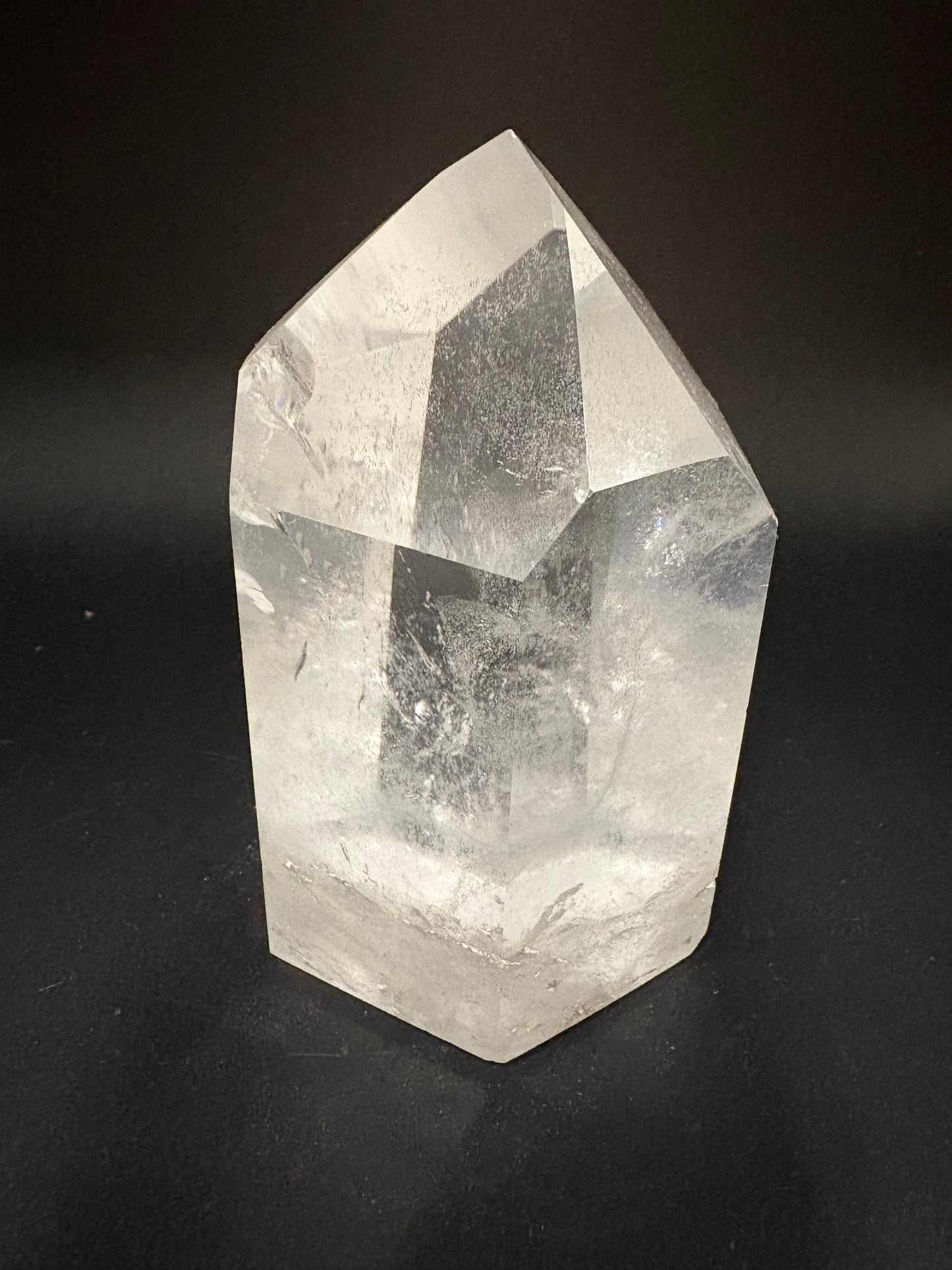 A faceted clear quartz crystal point with natural internal inclusions, photographed on a dark black background.