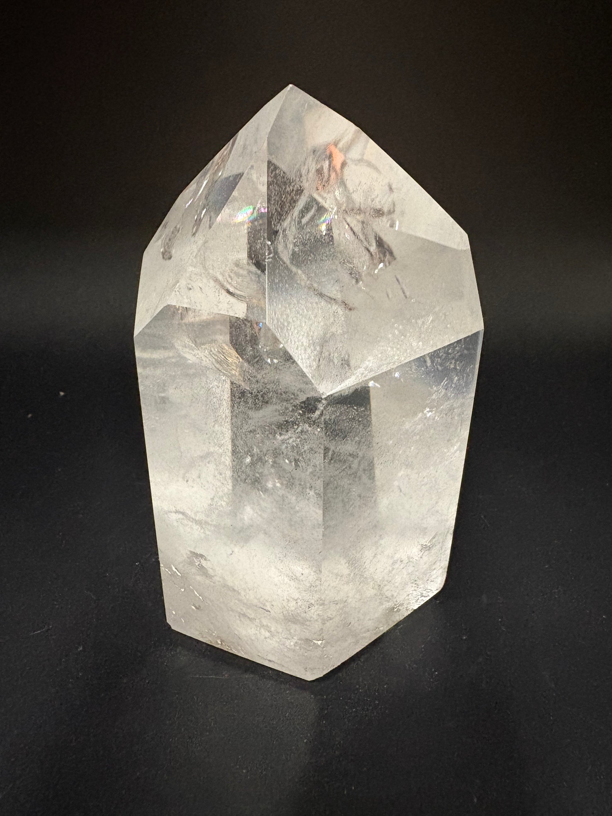 A faceted clear quartz crystal point with natural inclusions, displayed on a dark black background.