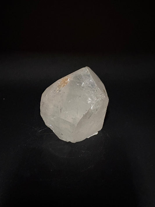 A rough, unpolished translucent crystal with a pale gray and white appearance, resting on a solid black background.