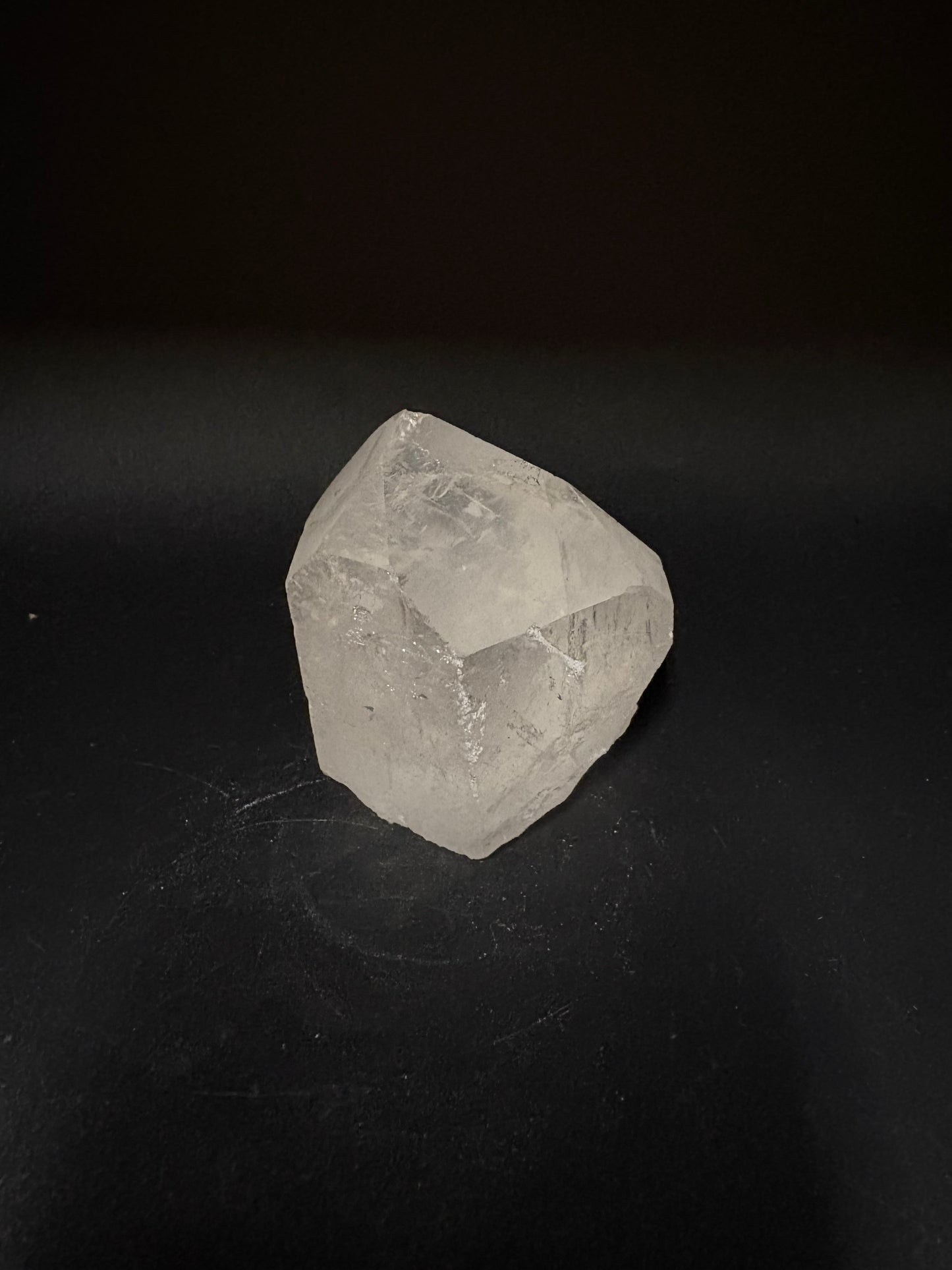 A raw, unpolished clear quartz crystal with natural geometric facets, displayed on a dark black background.