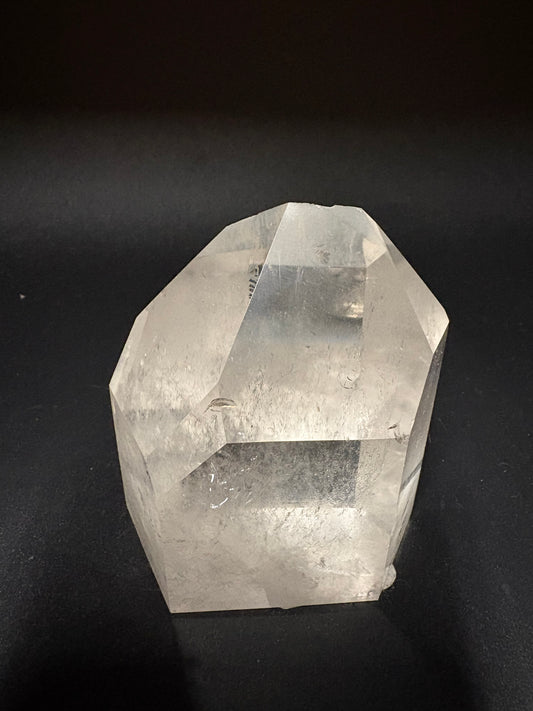 A natural clear quartz crystal point with visible internal inclusions and rough outer edges, photographed on a dark black background.
