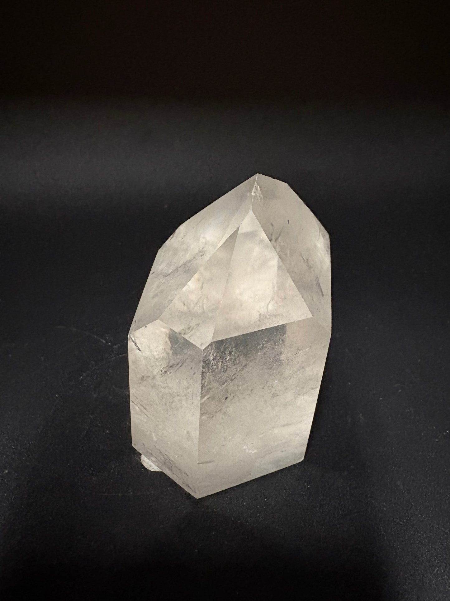 A faceted clear quartz crystal point resting on a dark, textured background.