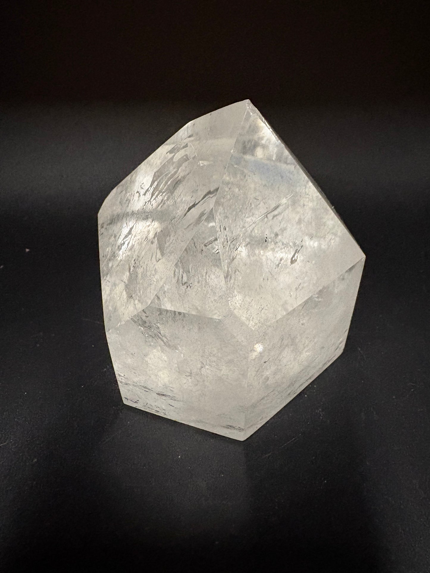 A faceted clear crystal stone, resembling a rough rose quartz or quartz crystal, photographed on a dark black background.