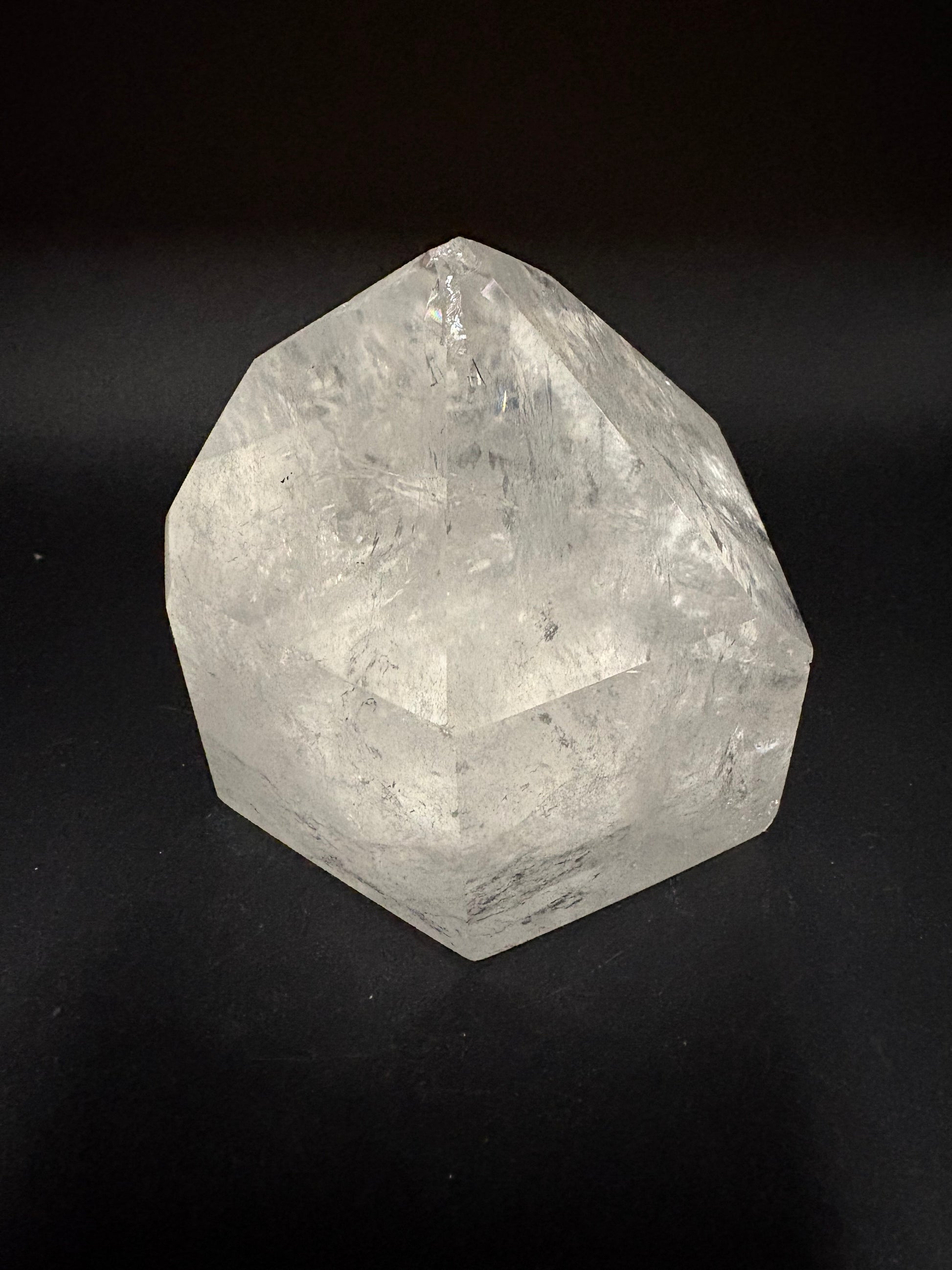 A faceted clear crystal stone, resembling a miniature quartz gem or polished geometric ornament, photographed on a solid black background.