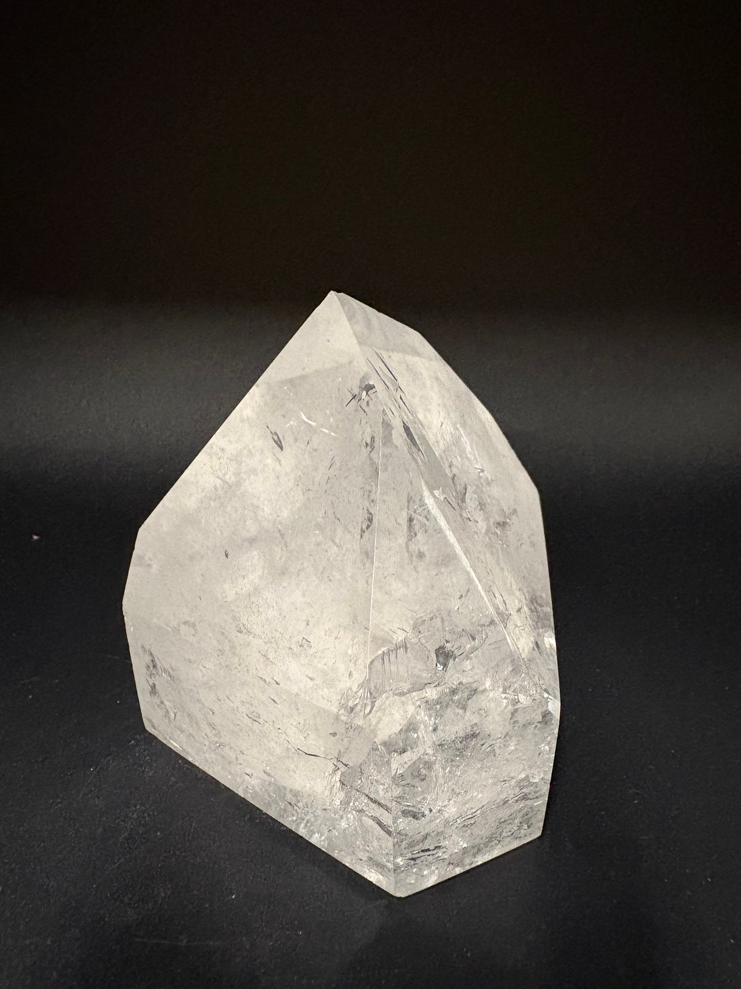 A faceted clear quartz crystal with natural inclusions, photographed on a dark black background.