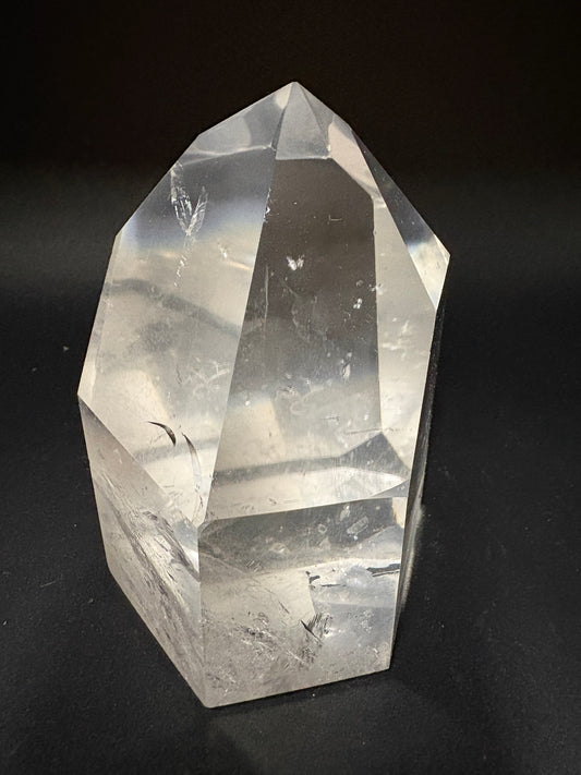 A clear faceted crystal point, likely quartz, resting on a dark black background.