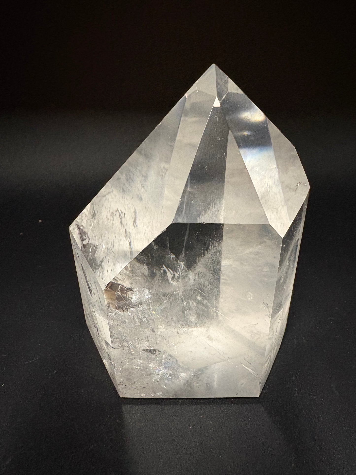 A clear faceted crystal point, likely quartz, displayed on a dark black background.