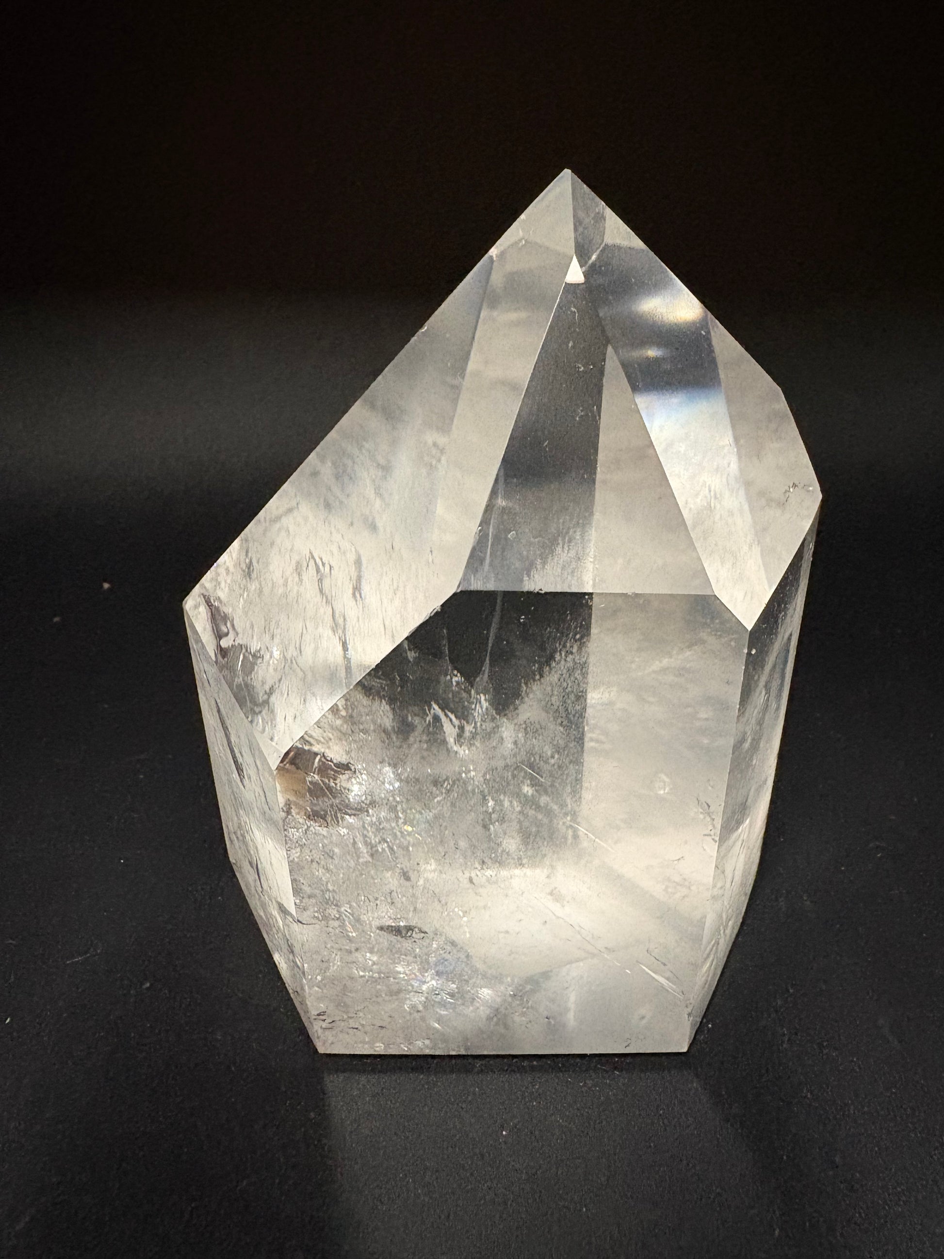 A clear faceted crystal point, likely quartz, displayed on a dark black background.