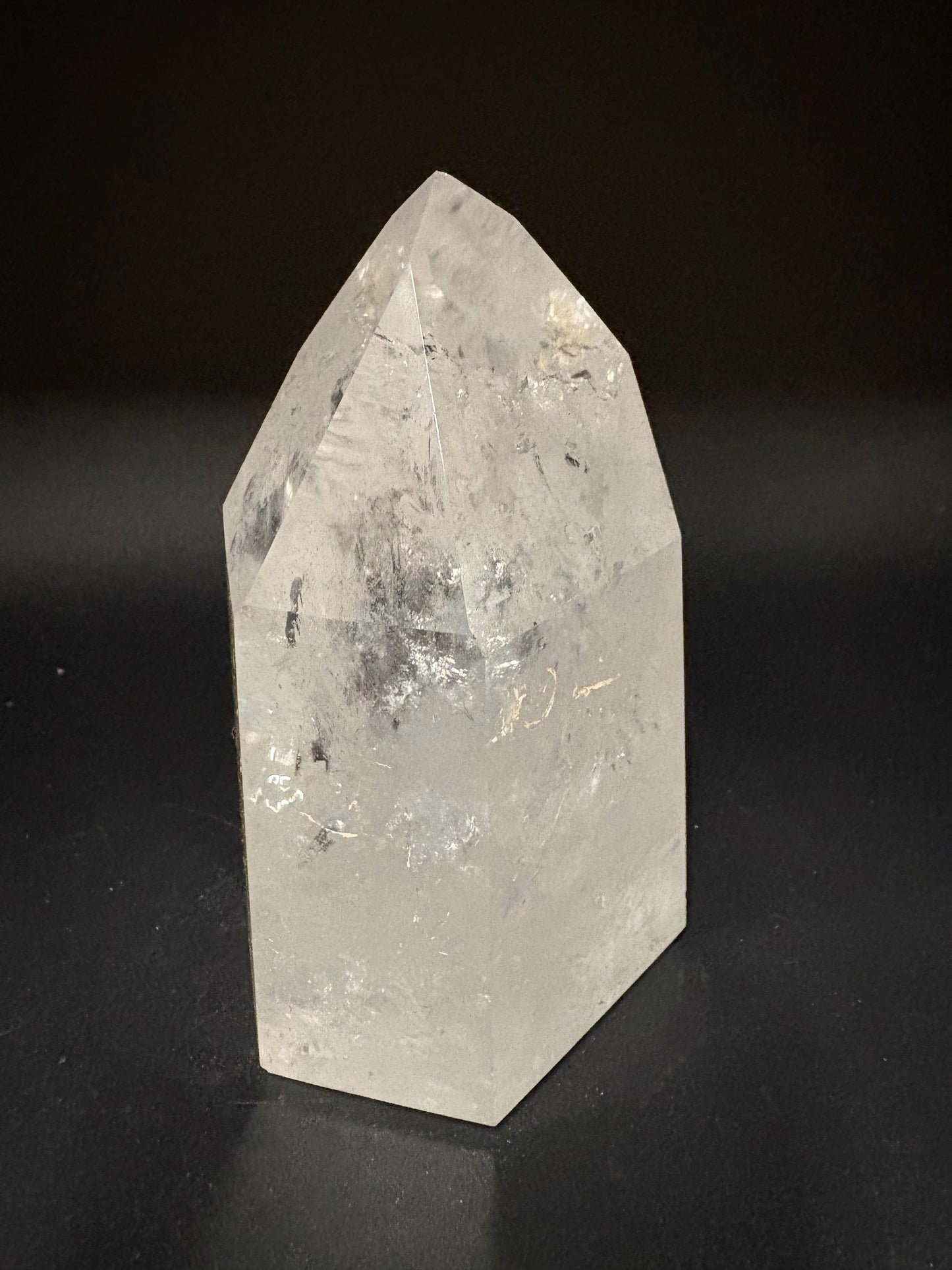 A natural clear quartz crystal point with internal inclusions, displayed on a dark black background.