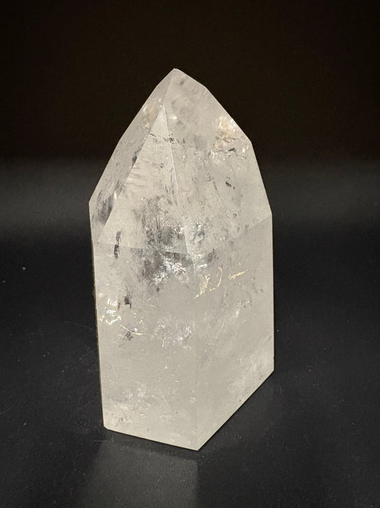 A natural clear quartz crystal point with internal inclusions, displayed on a dark black background.