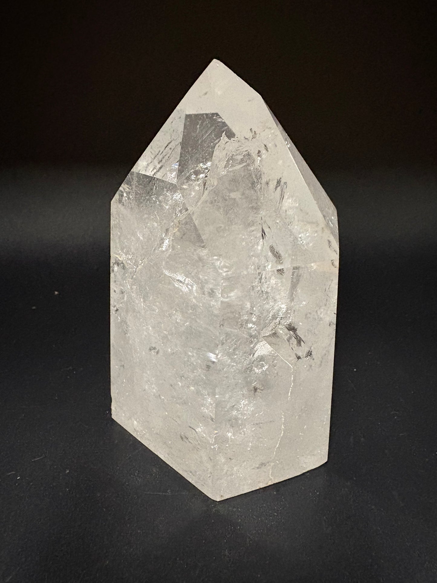 A raw, pointed crystal mineral specimen with natural facets and internal inclusions, shown on a dark black background.