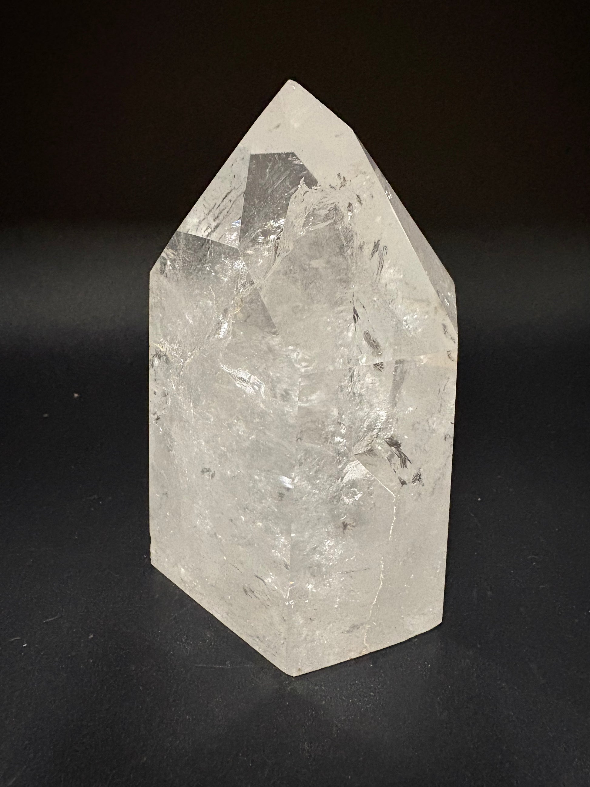 A raw, pointed crystal mineral specimen with natural facets and internal inclusions, shown on a dark black background.