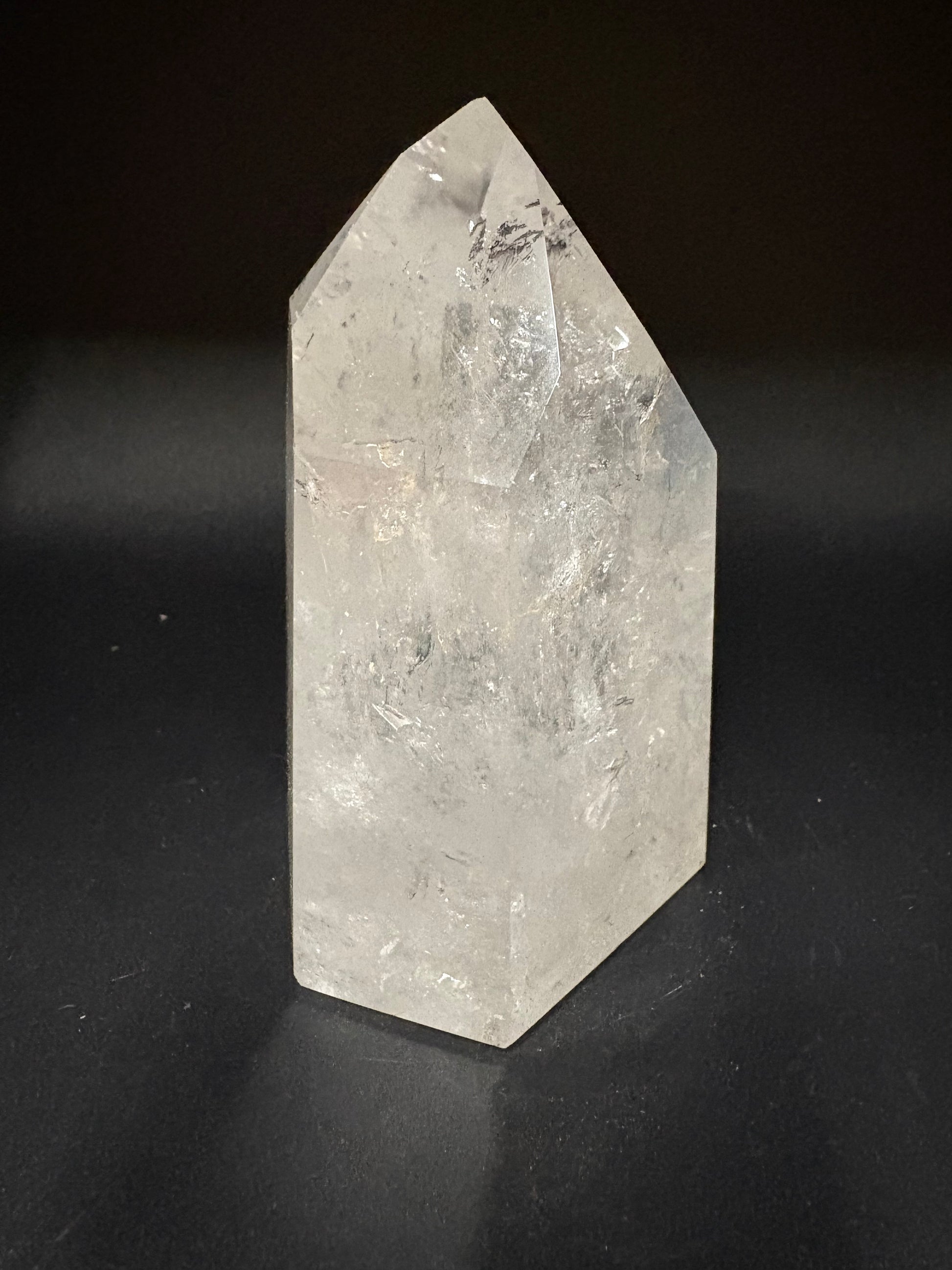 A raw, pointed clear quartz crystal with natural inclusions, resting on a dark black background.