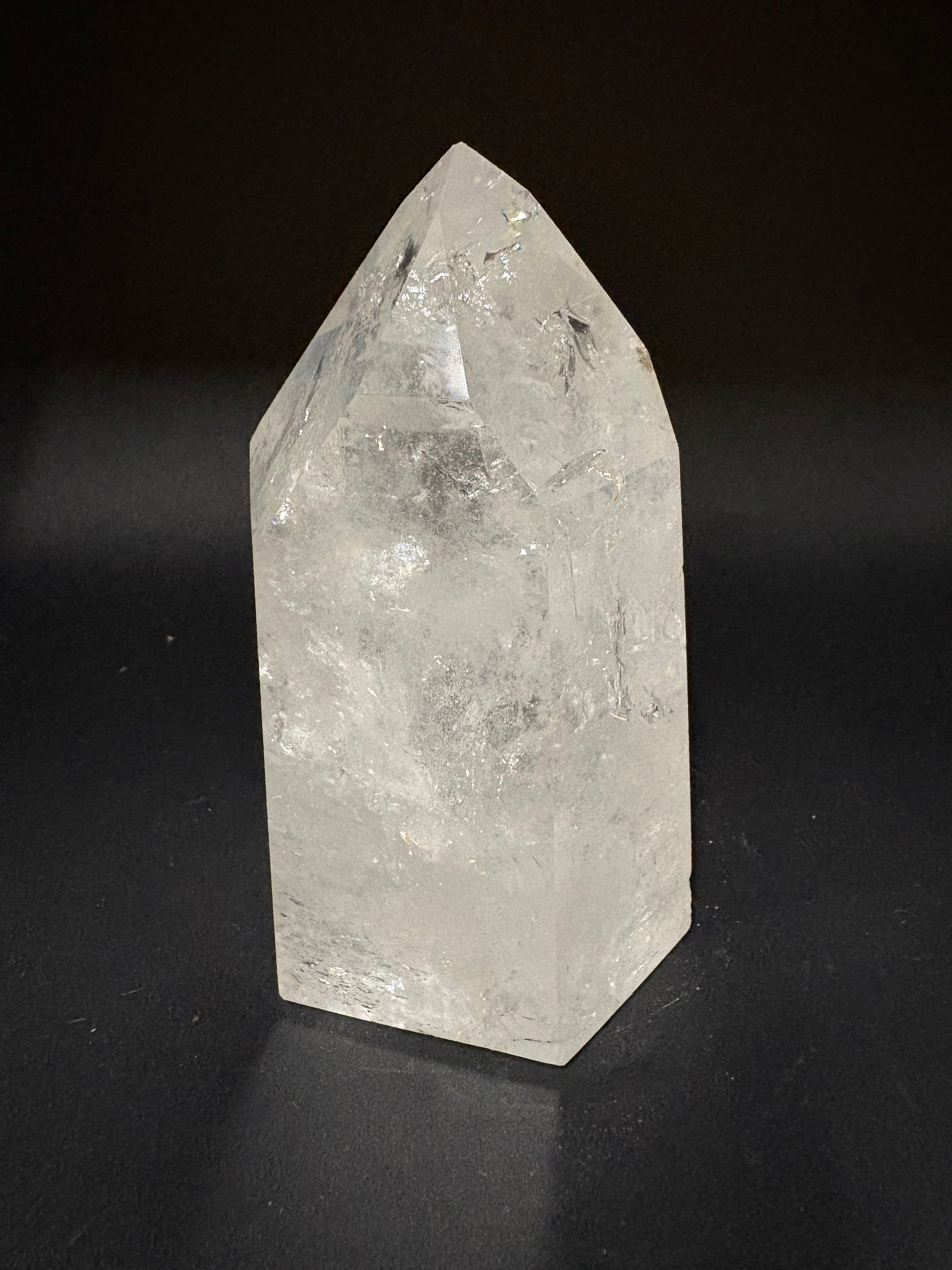 A raw, pointed clear quartz crystal with natural inclusions, displayed on a dark black background.