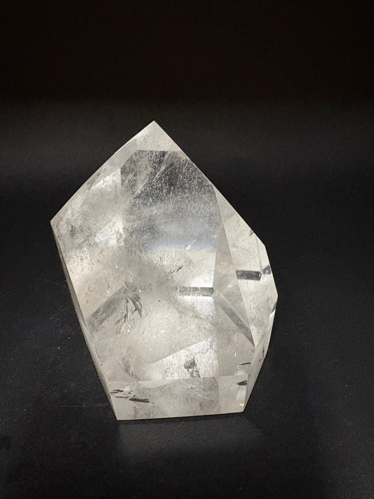 A faceted clear quartz crystal point with internal inclusions, displayed on a dark black background.