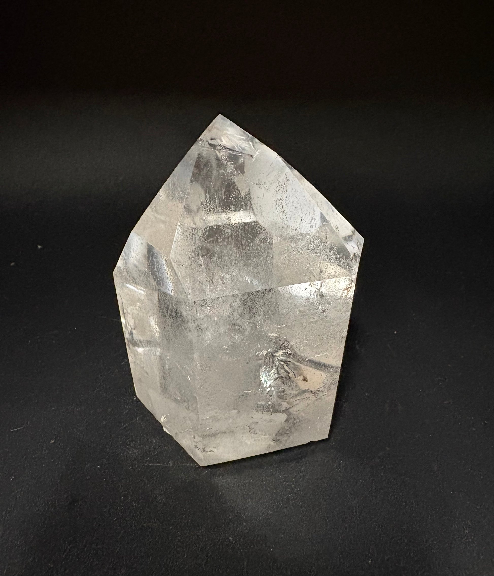 A clear faceted crystal tower or point-shaped stone sculpture with natural internal inclusions, photographed on a dark black background.