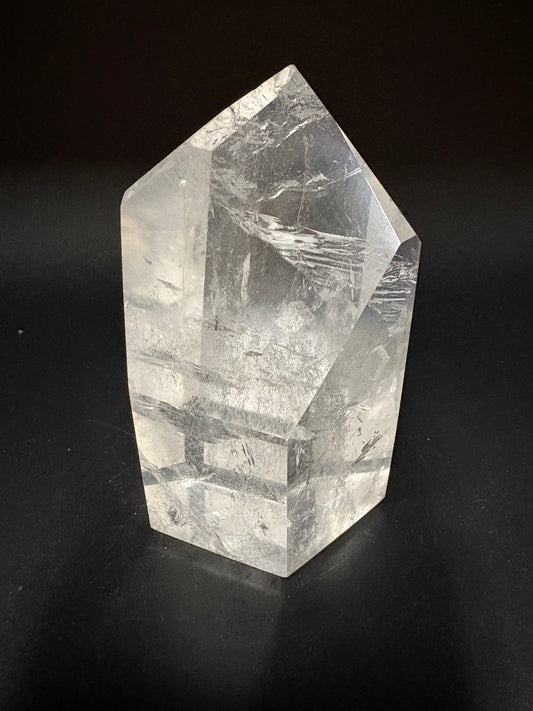 A clear faceted crystal point, likely quartz, displayed on a solid black background.
