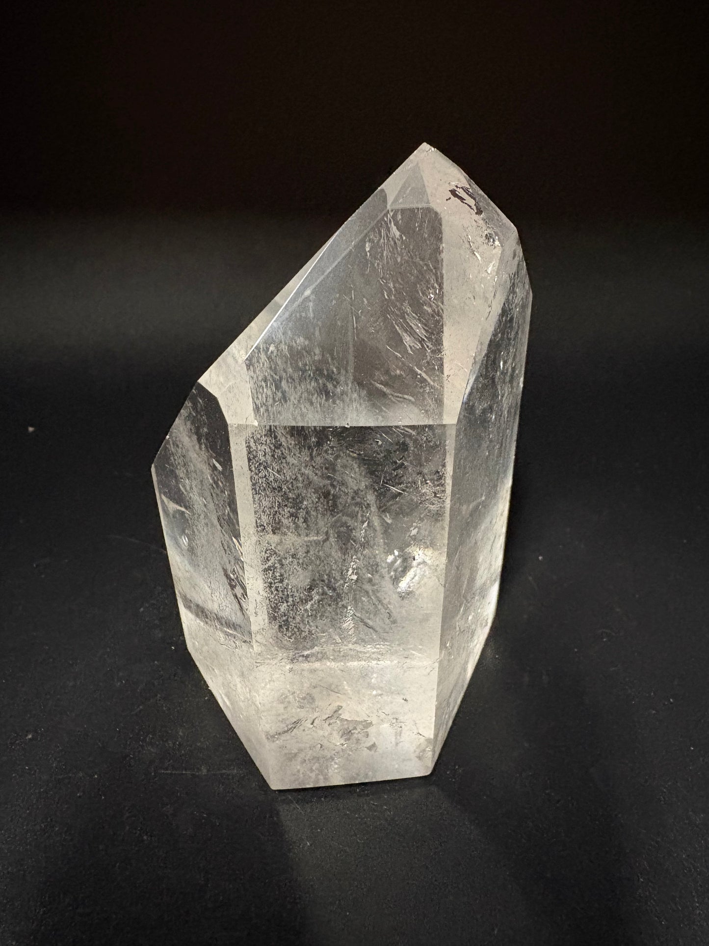 A clear quartz crystal point with visible internal inclusions, photographed on a dark black background.